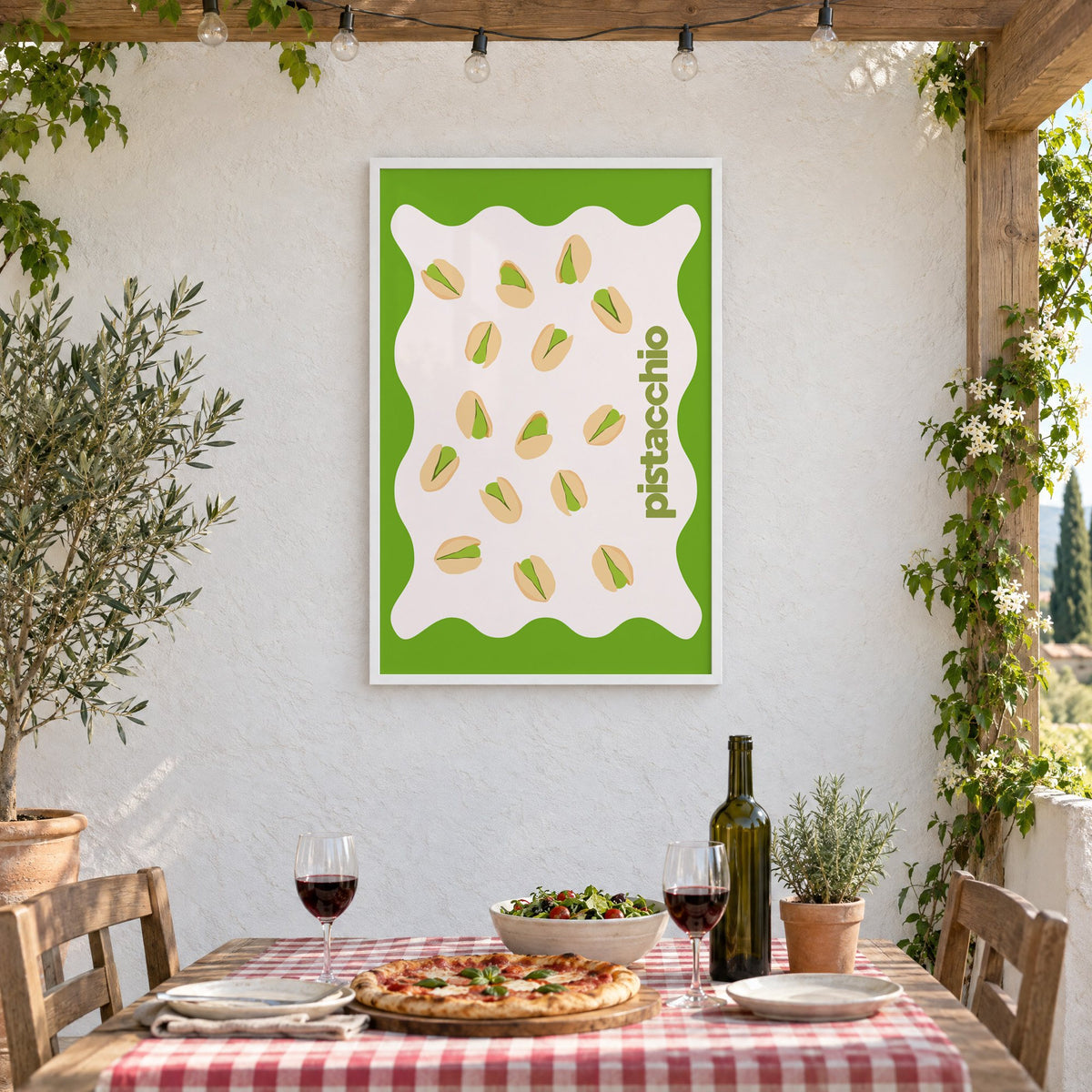 pistacchio vertical type pistachio nuts print in a white frame on a stucco wall above a checked-cloth table with pizza and red wine