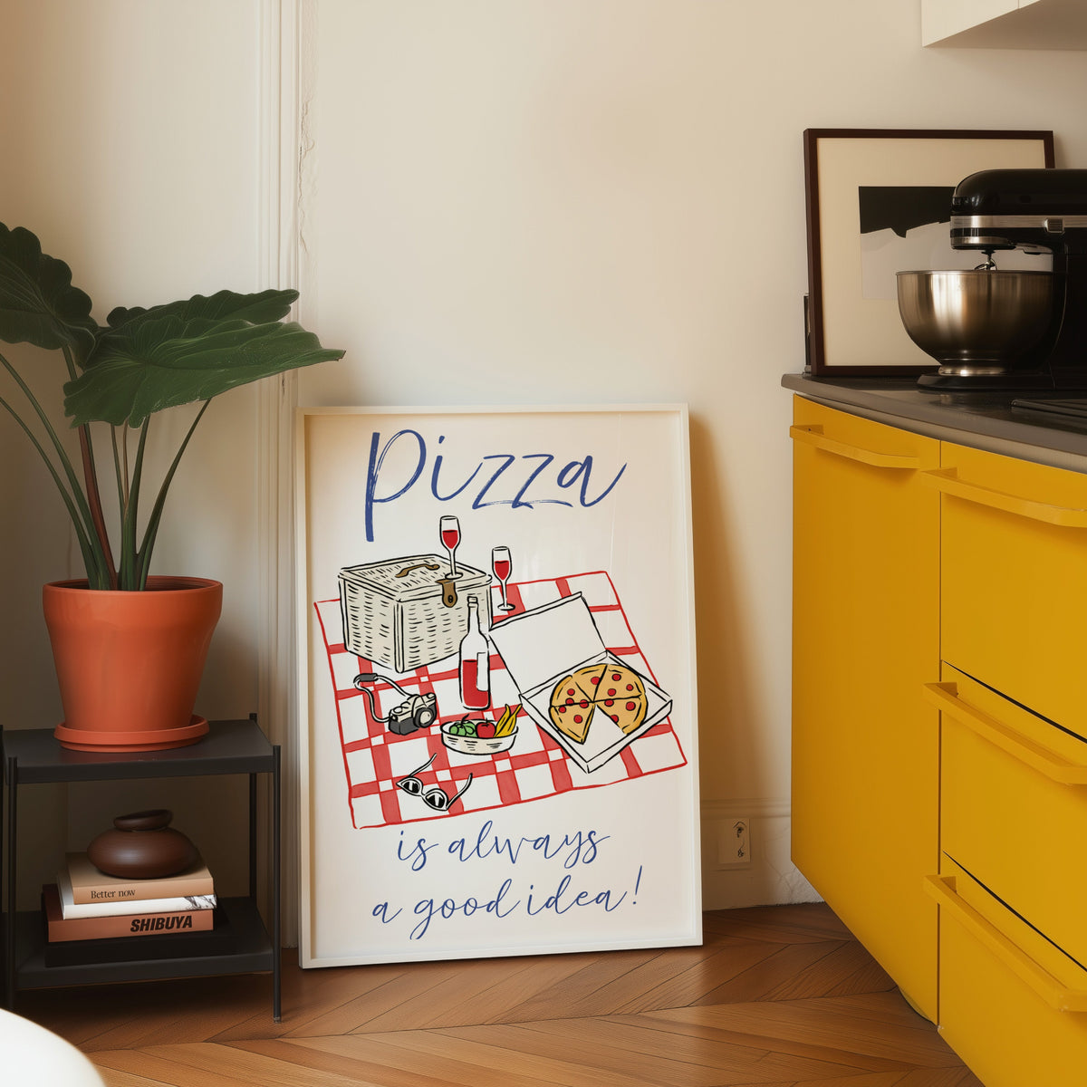 Pizza picnic print in a white frame leaning on parquet beside a yellow kitchen