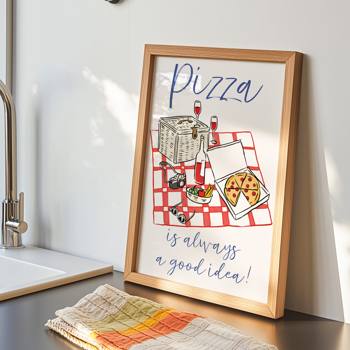 Pizza picnic print in an oak frame by the kitchen sink beside a striped tea towel