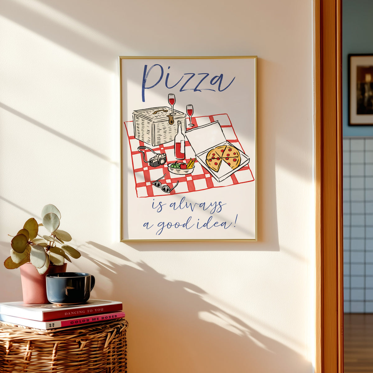 Pizza picnic print in a gold frame above a basket of books and a pilea plant