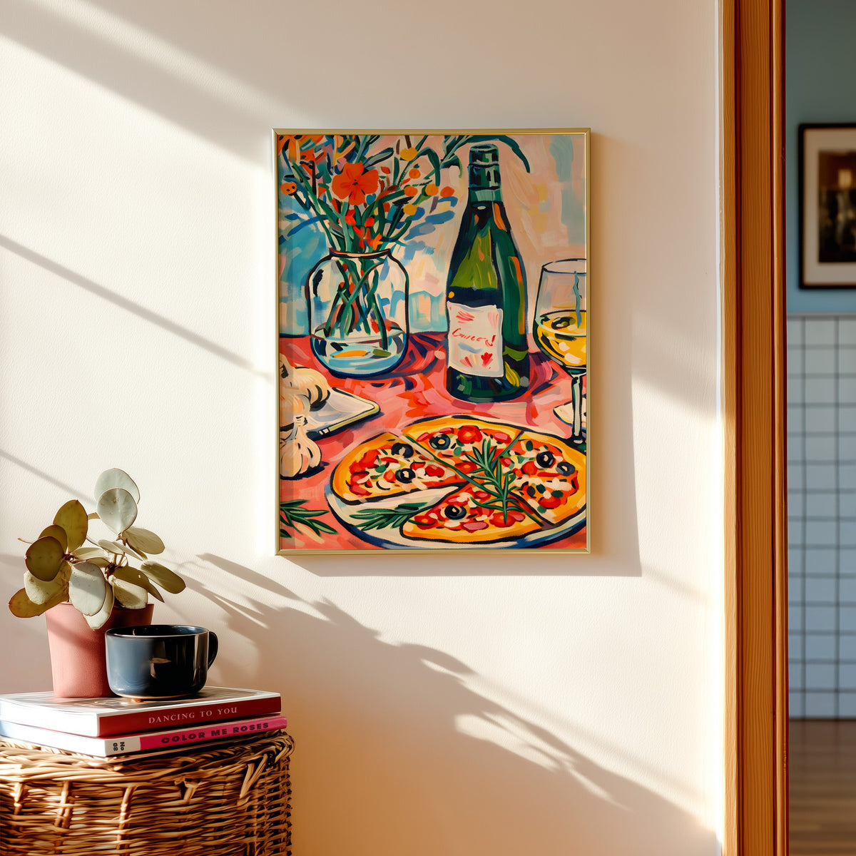 Pizza and champagne print in a gold frame above a basket of books and a pilea plant