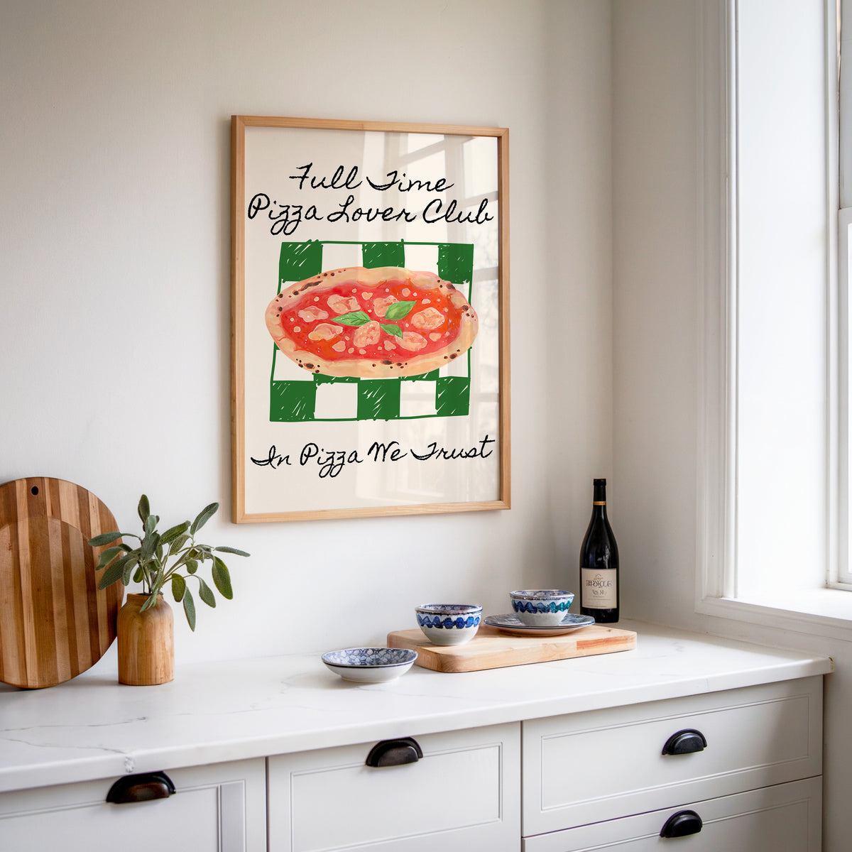 Pizza Lover Club green check print in an oak frame above a white kitchen sideboard with a wine bottle and wooden board