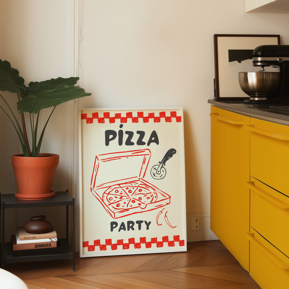 Pizza Party print in a white frame leaning on parquet beside a yellow kitchen