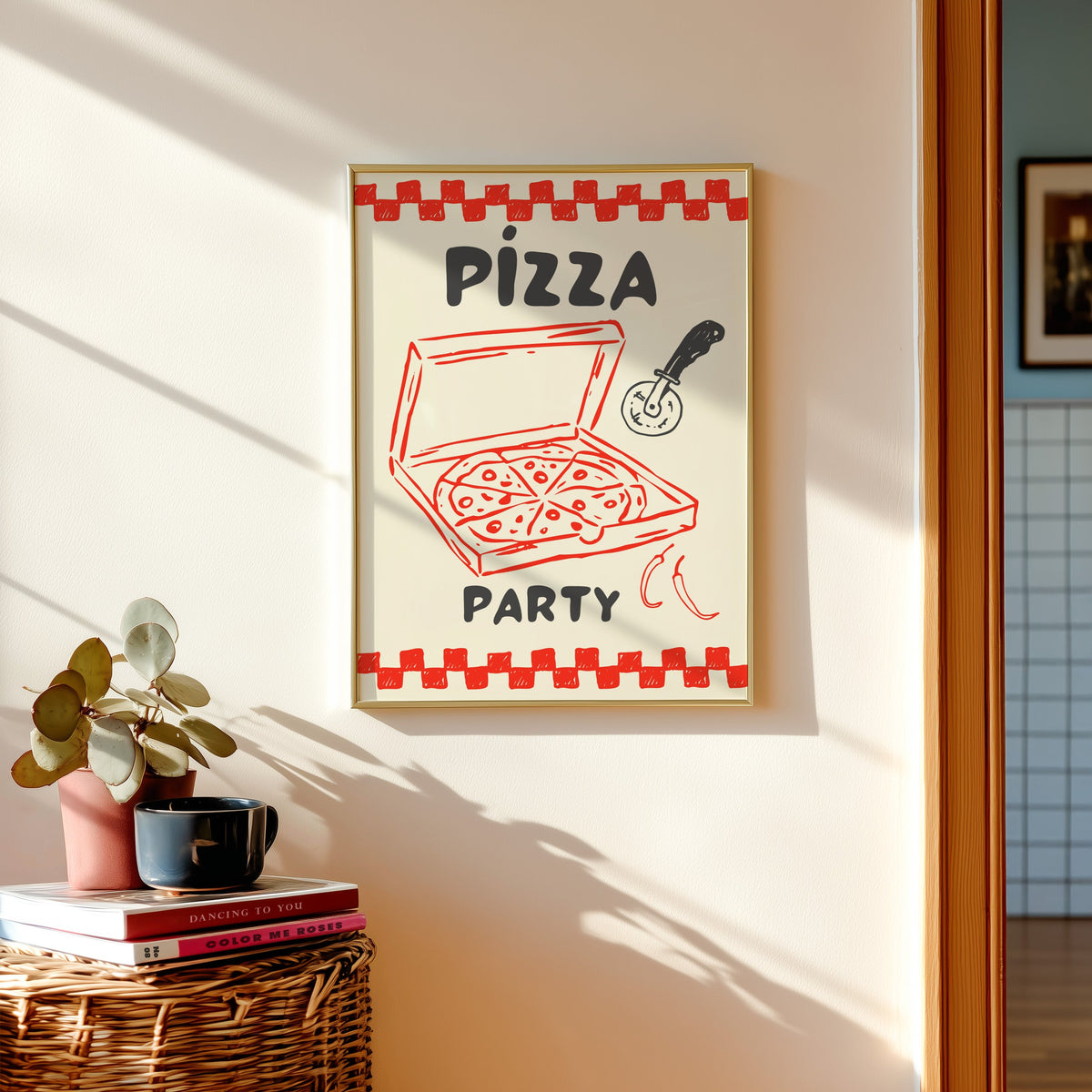 Pizza Party print in a gold frame above a basket of books and a pilea plant