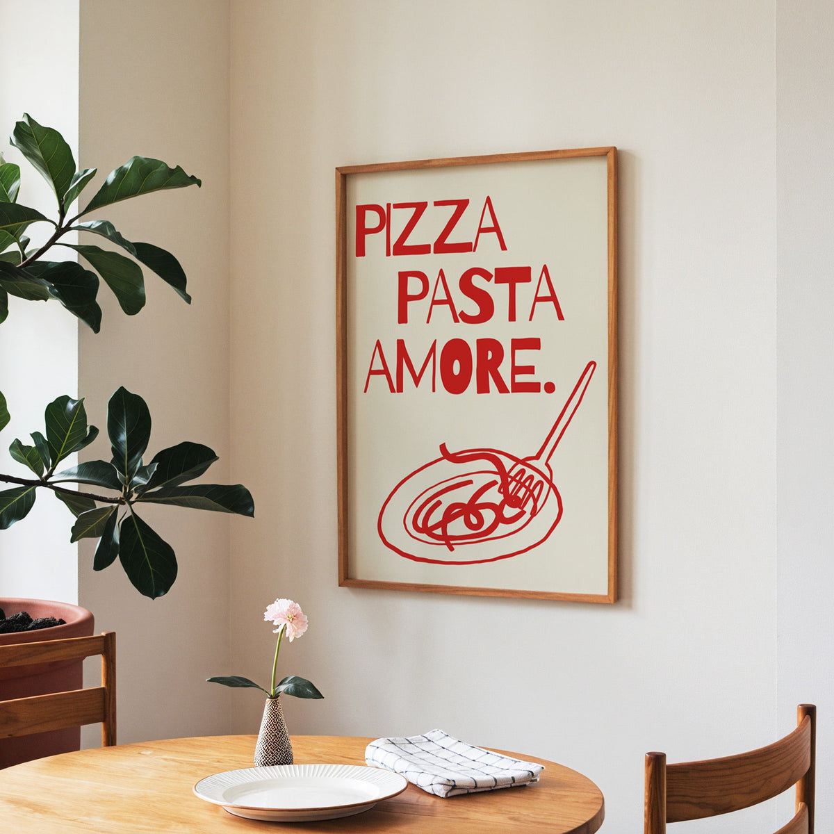 Pizza Pasta Amore print in a walnut frame above a round table beside a fiddle-leaf fig