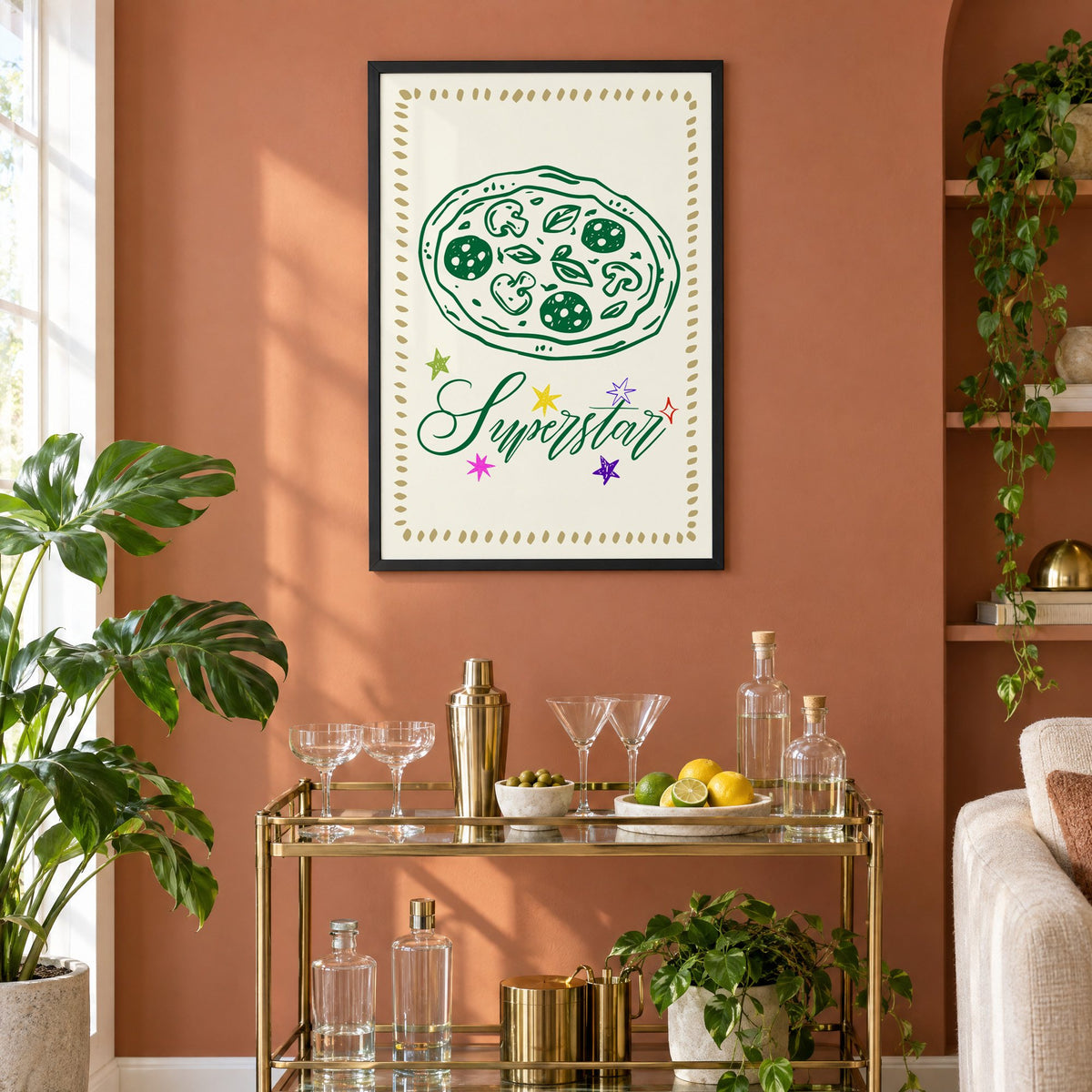 Superstar green pizza and stars print in a black frame on a terracotta wall above a brass bar cart with coupes and citrus