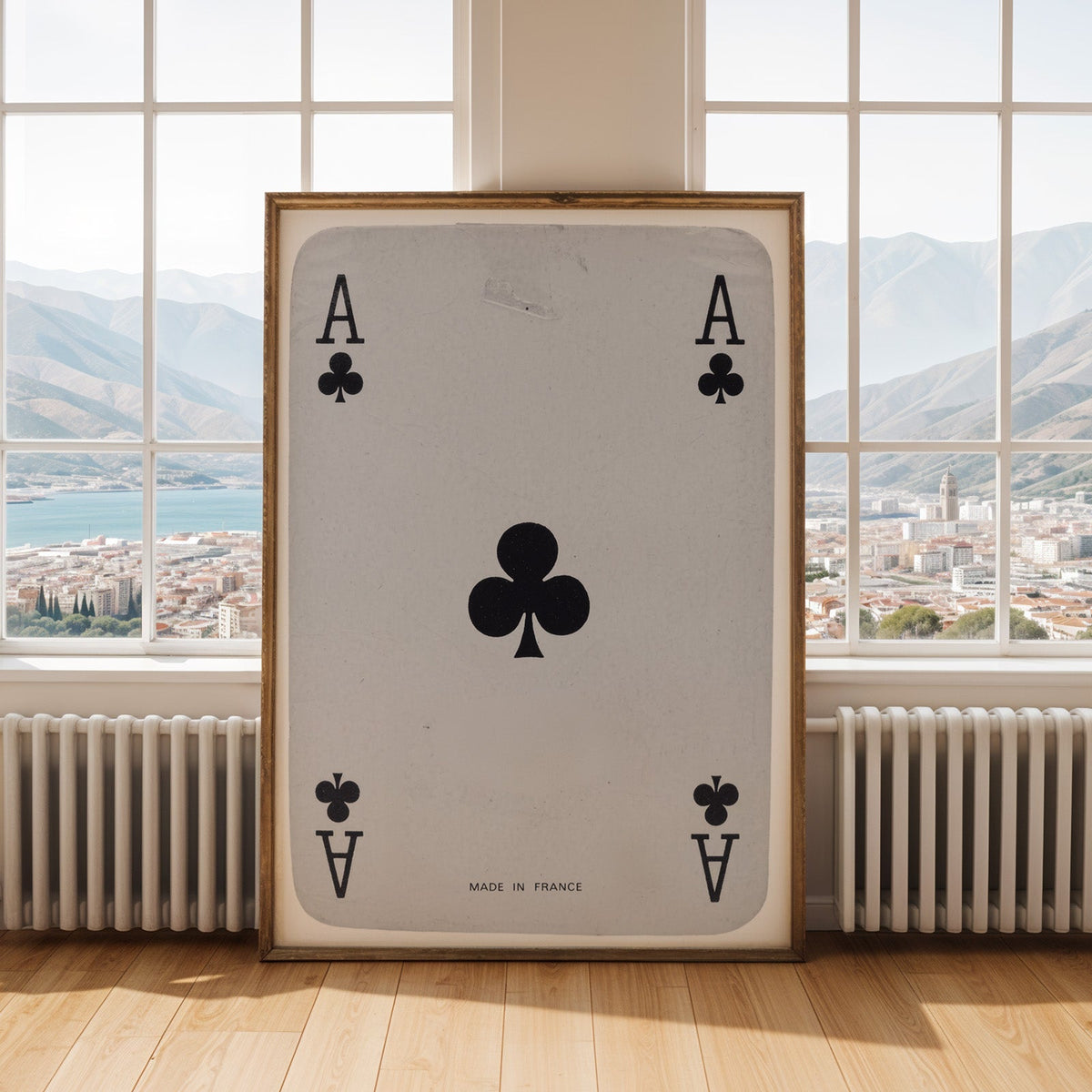 Worn vintage ace of clubs playing card print shown in an antique gold frame by tall windows with a sea view