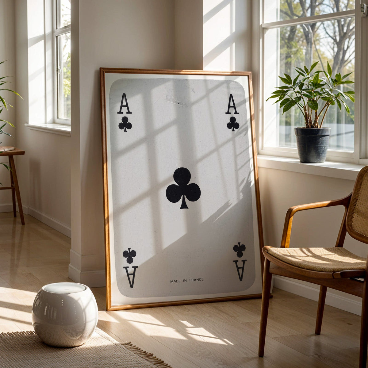 Worn vintage ace of clubs playing card print in a walnut frame on a wood floor beside a cane chair and sunny window