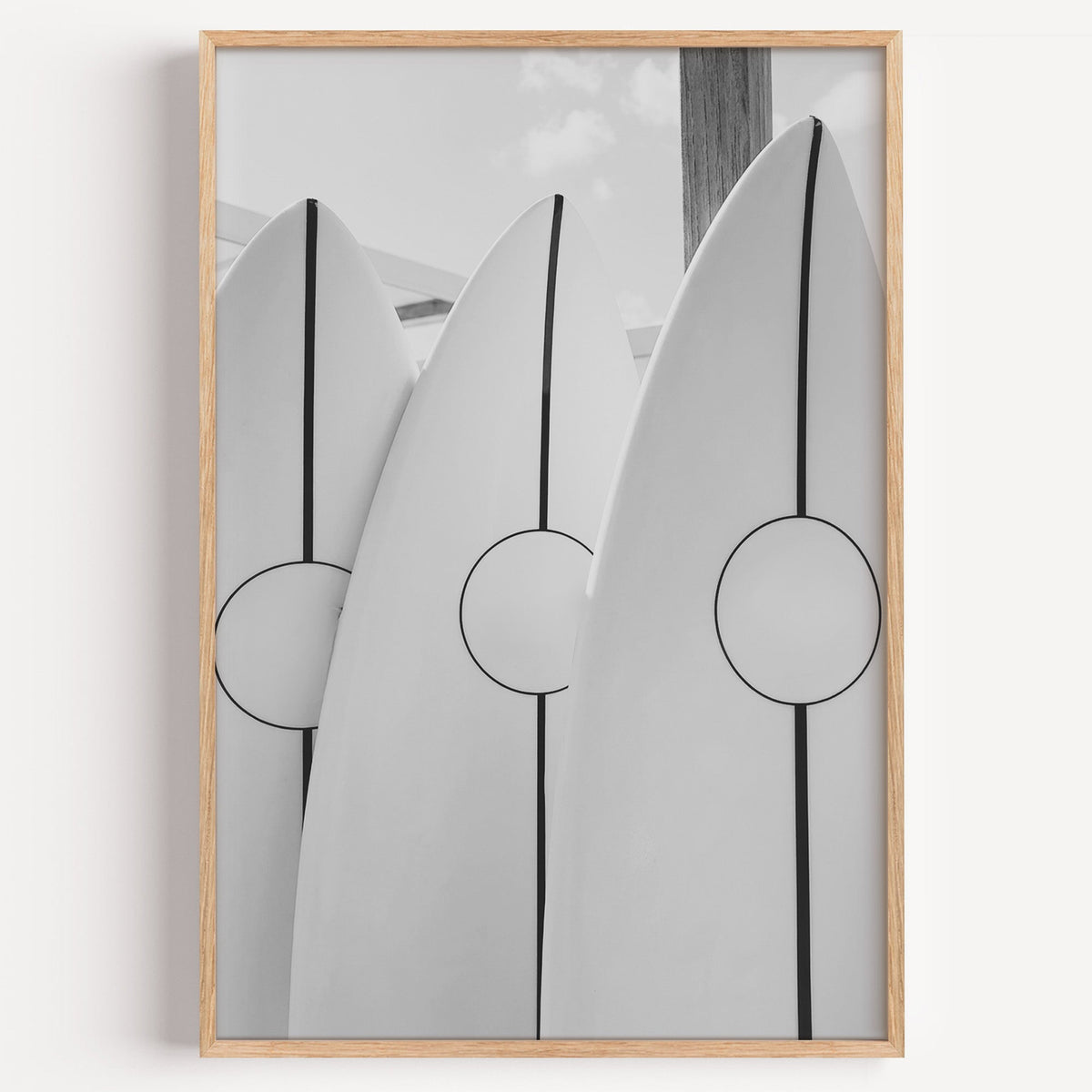 Three white surfboards with black stripes print in a light oak frame on a plain white wall