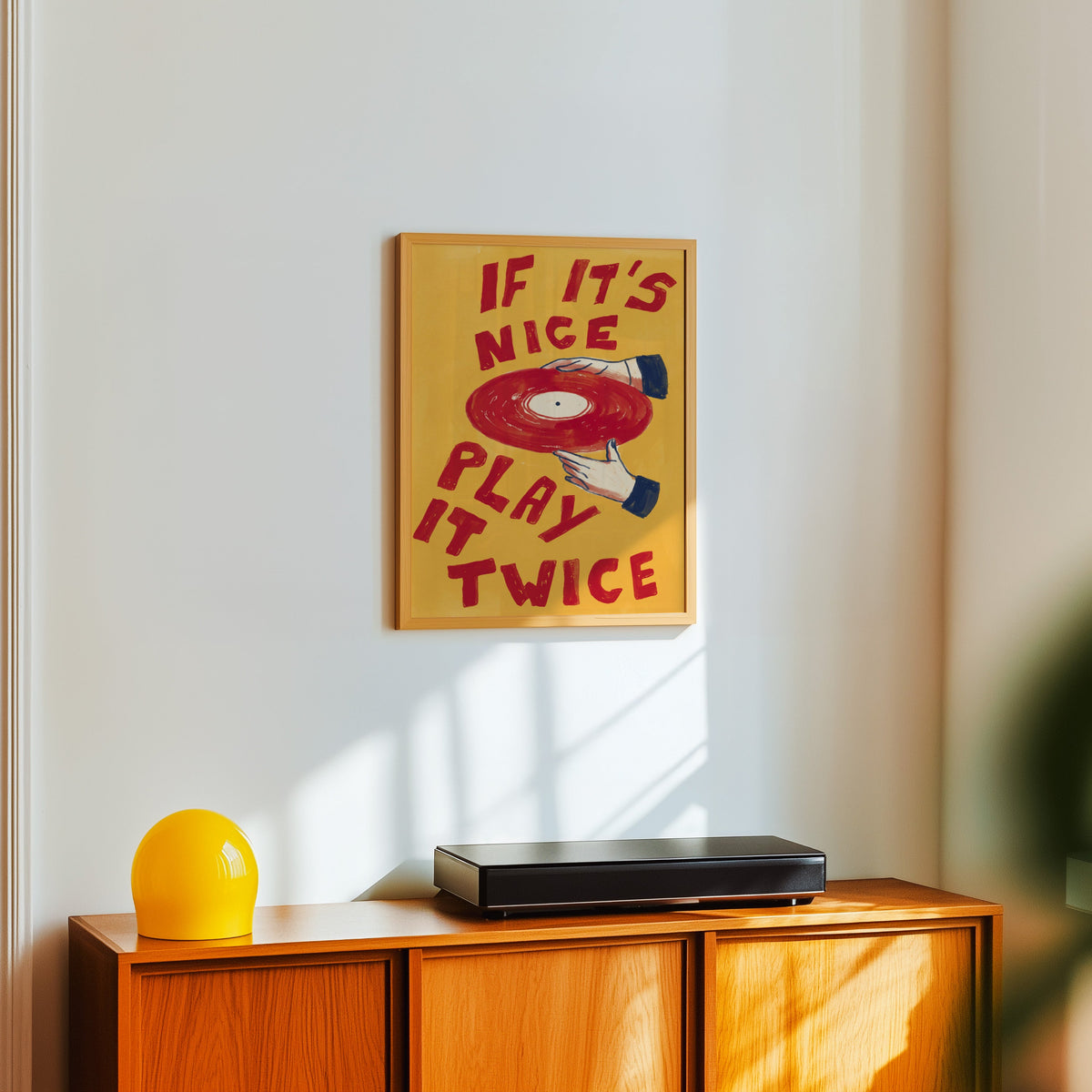 Retro music quote print in a light oak frame above a teak sideboard with a yellow lamp