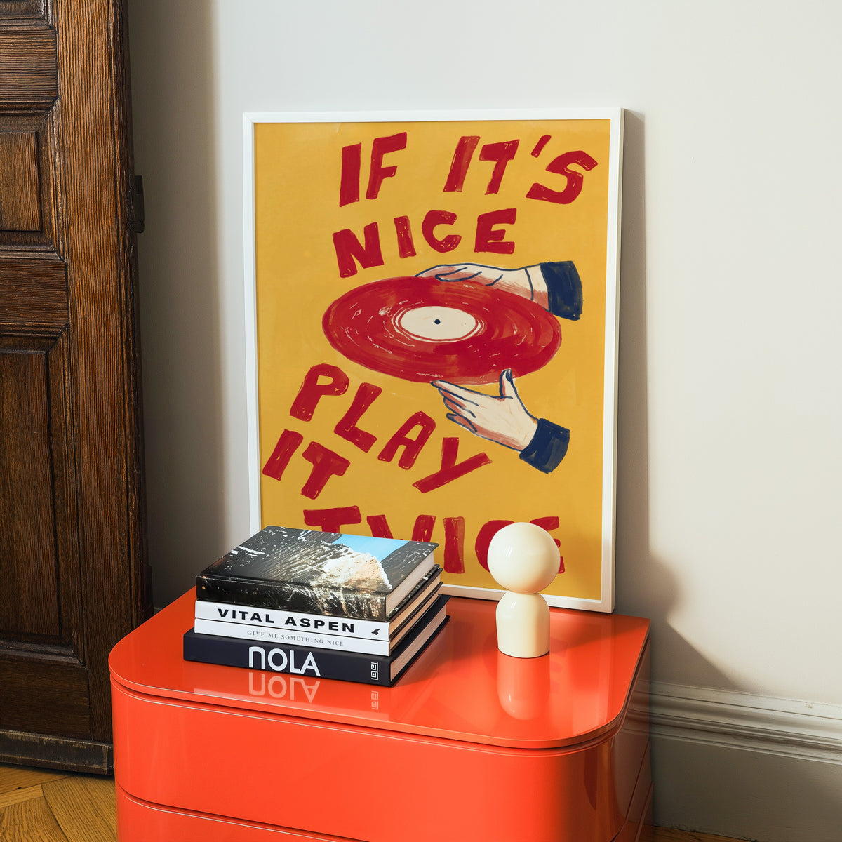 Vinyl record typography print in a white frame on a glossy orange cabinet with books