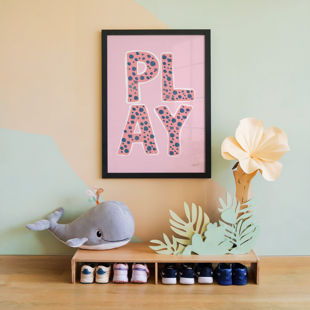 Spotted play letters pink nursery print in a black frame on a mint and peach wall above a whale plush