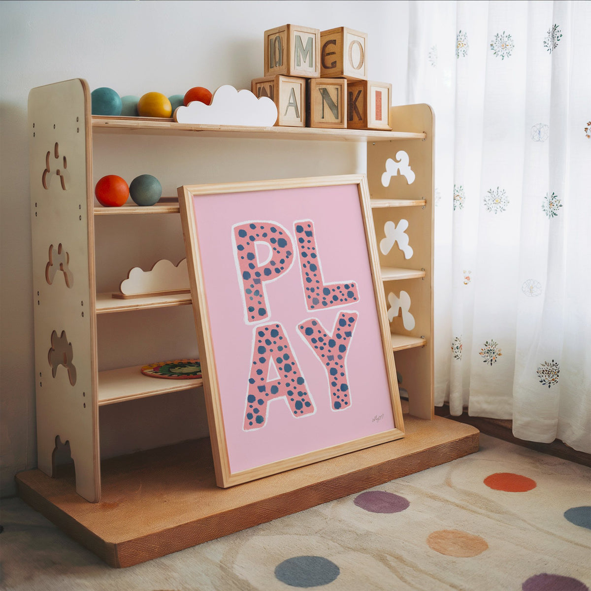Spotted play letters pink nursery print in an oak frame leaning on a toy shelf with wooden letter blocks
