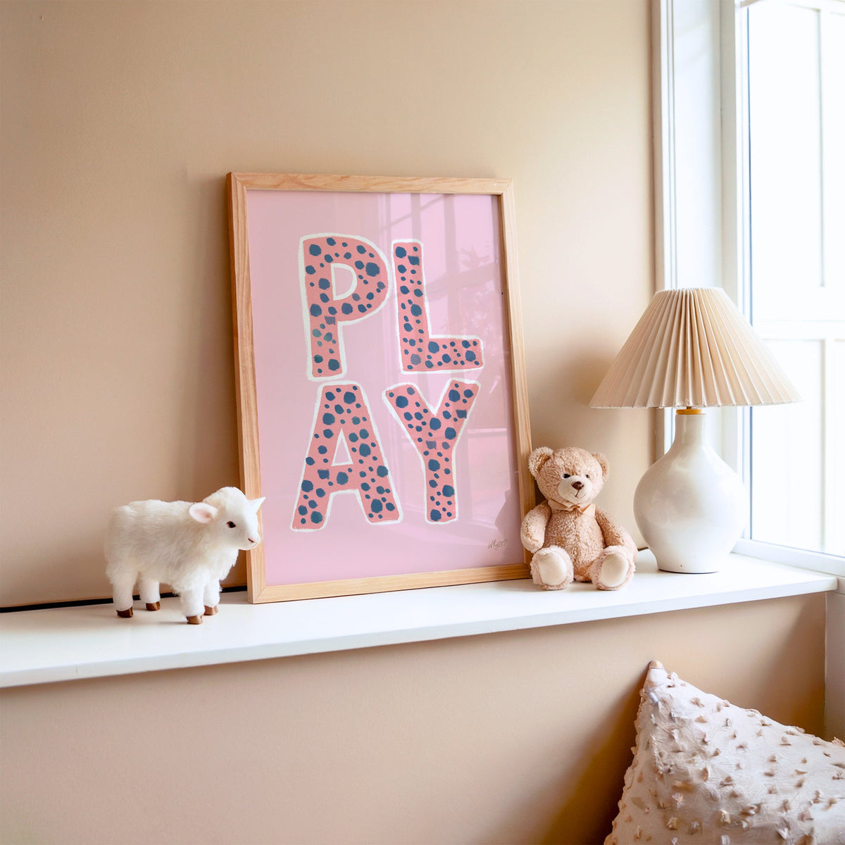 Spotted play letters pink nursery print in an oak frame on a window ledge with a toy lamb and teddy