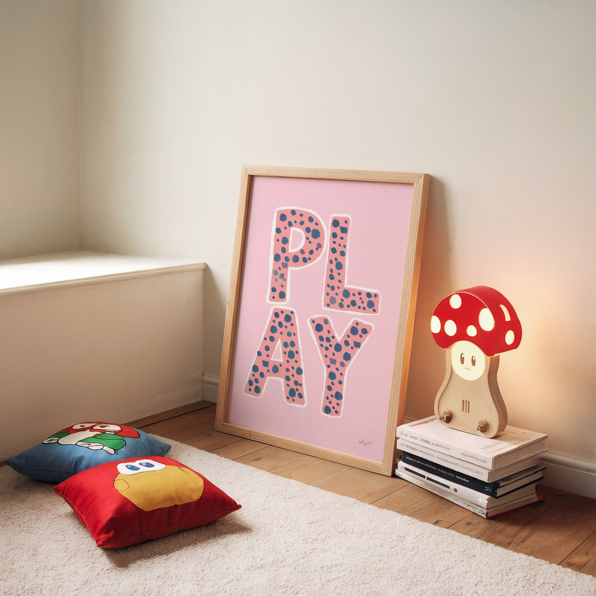 Spotted play letters pink nursery print in an oak frame leaning on a rug beside a mushroom lamp and floor cushions