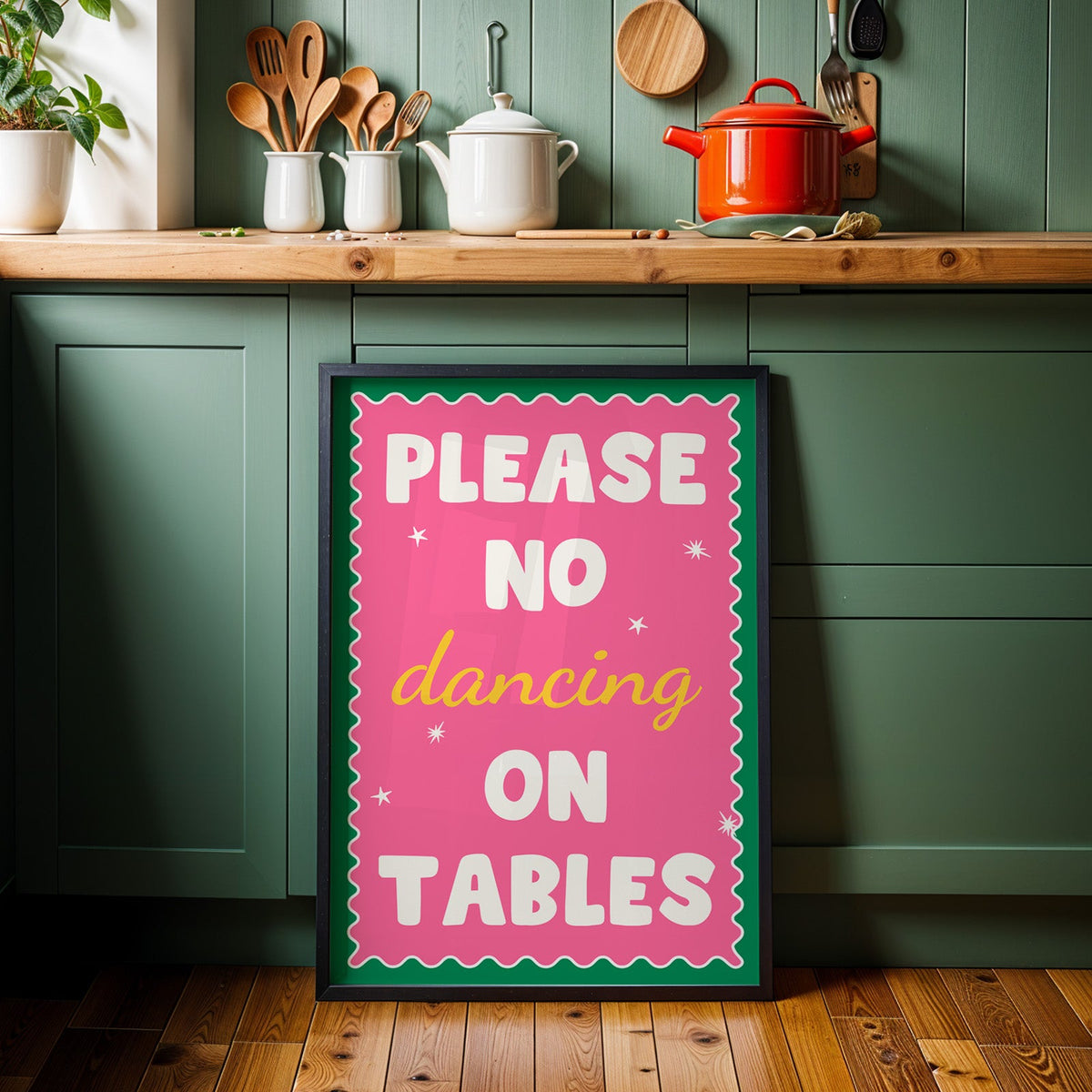 Please no dancing on tables print in a black frame against sage green kitchen cabinets