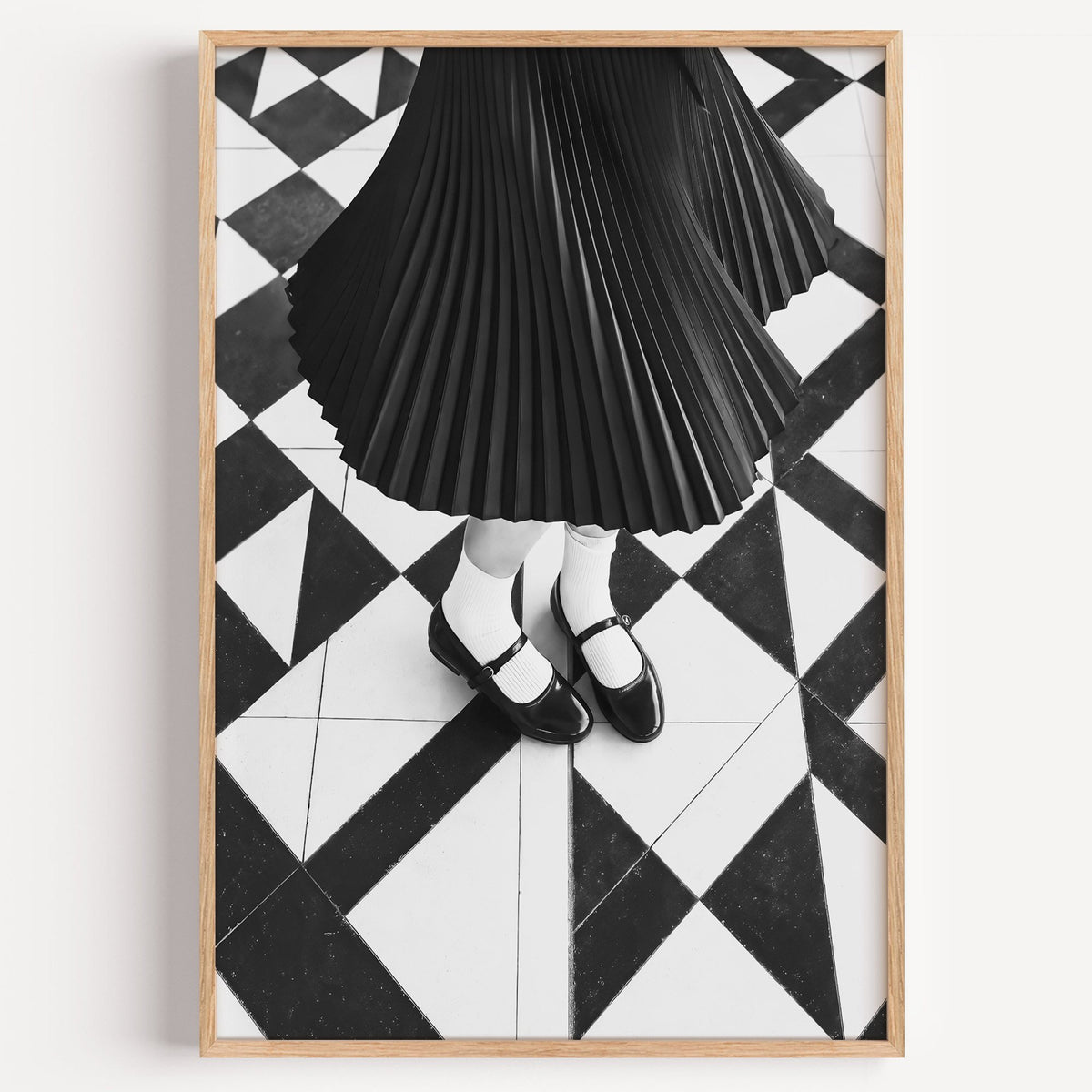 Pleated skirt and strap shoes on geometric tile print in a light oak frame on a plain white wall