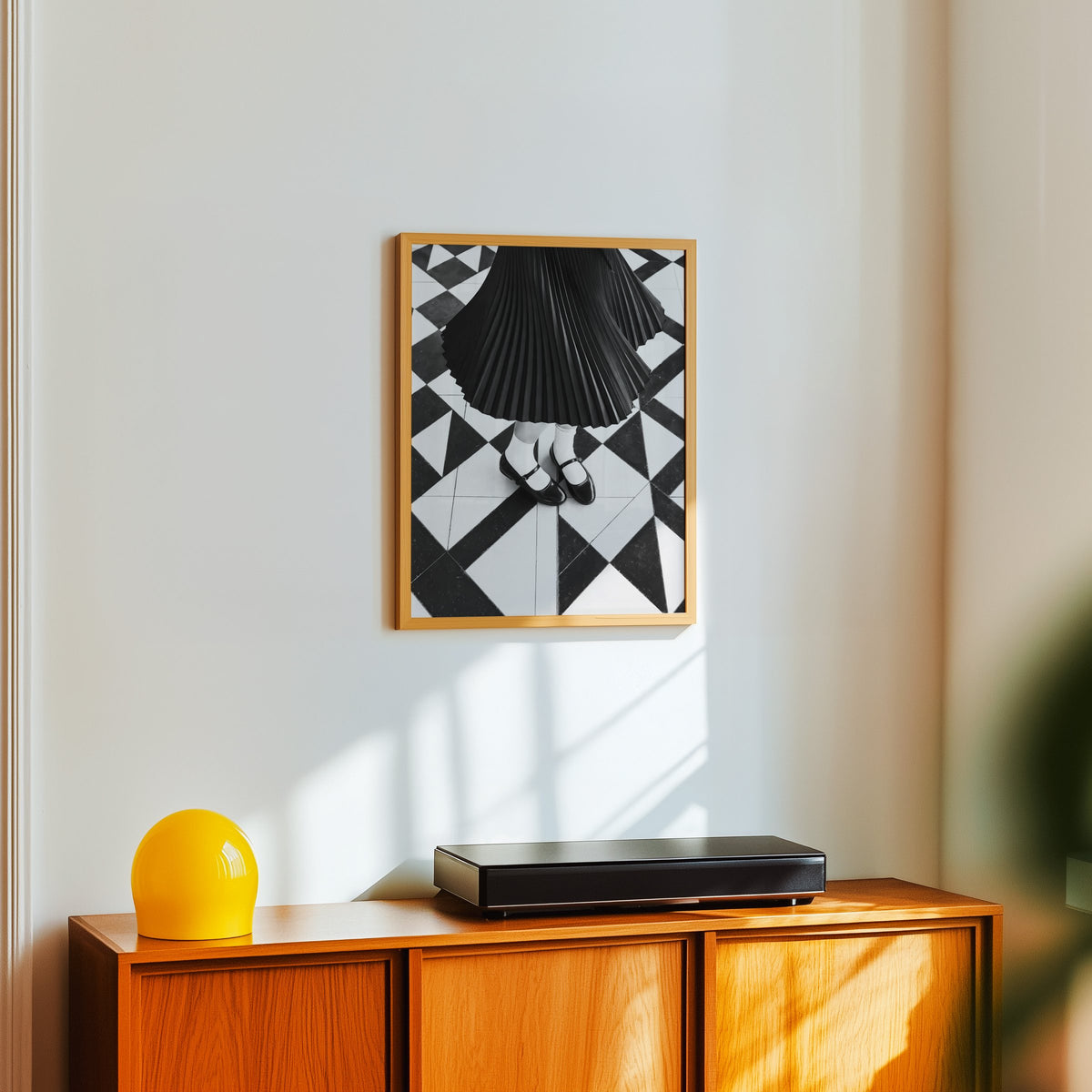 Pleated skirt and strap shoes on geometric tile print in an oak frame above a teak sideboard with a yellow glass lamp