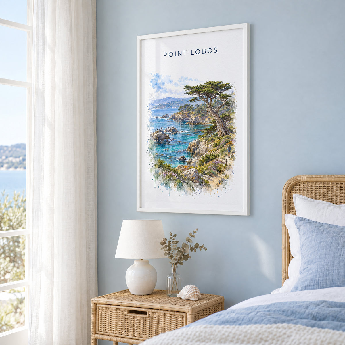 Point Lobos State Natural Reserve watercolor in a white frame on a pale blue wall beside a rattan bed in a coastal bedroom