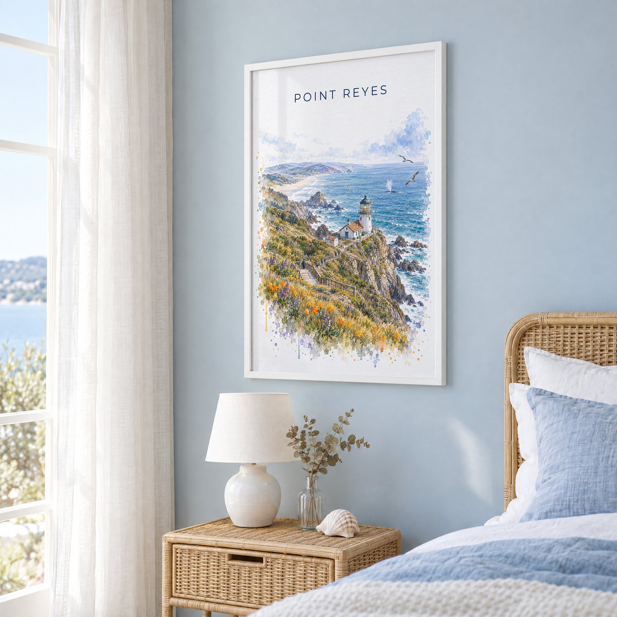 Point Reyes watercolor print in a white frame on a pale blue wall beside a rattan bed in a coastal bedroom