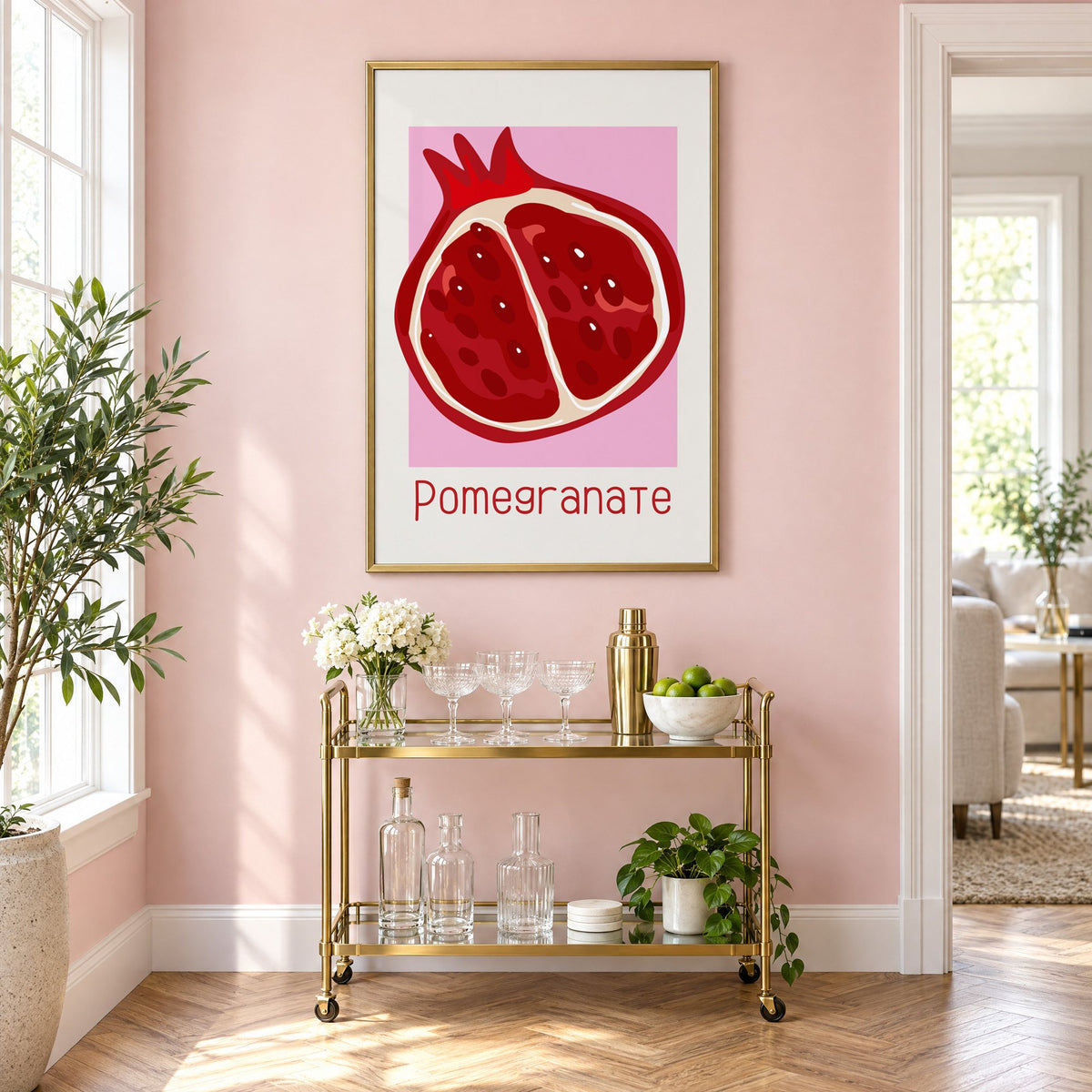 Pomegranate thin lettering halved fruit print in a brass frame on a blush pink wall above a gold bar cart with glassware