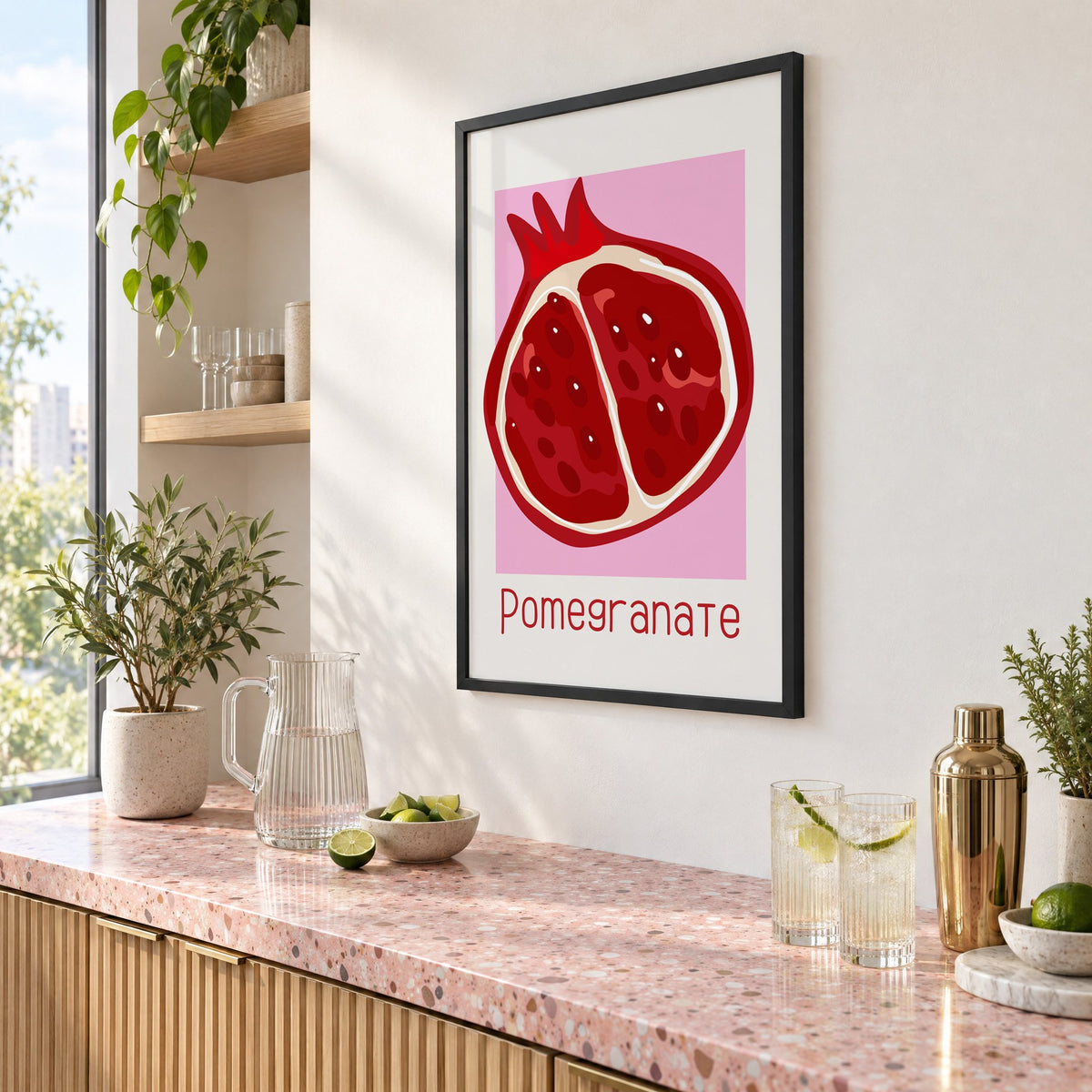Pomegranate thin lettering halved fruit print in a black frame above a pink terrazzo cocktail counter with limes, seen at an angle