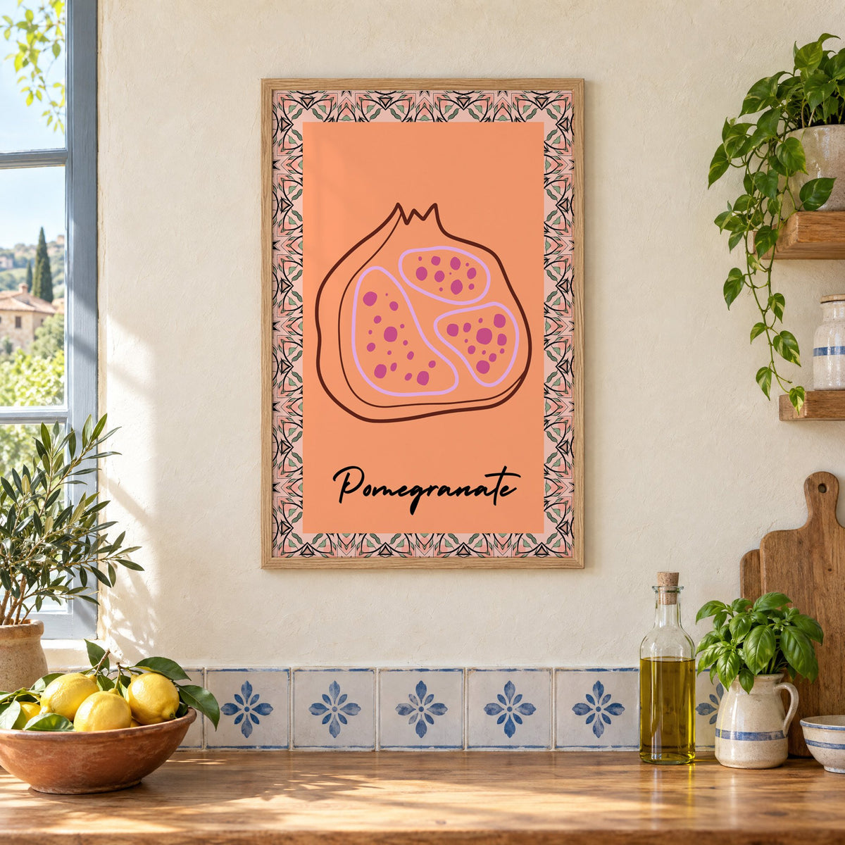 Pomegranate line-art kaleidoscope border print in an oak frame on a cream plaster wall above a worktop with a bowl of lemons and blue-and-white tiles