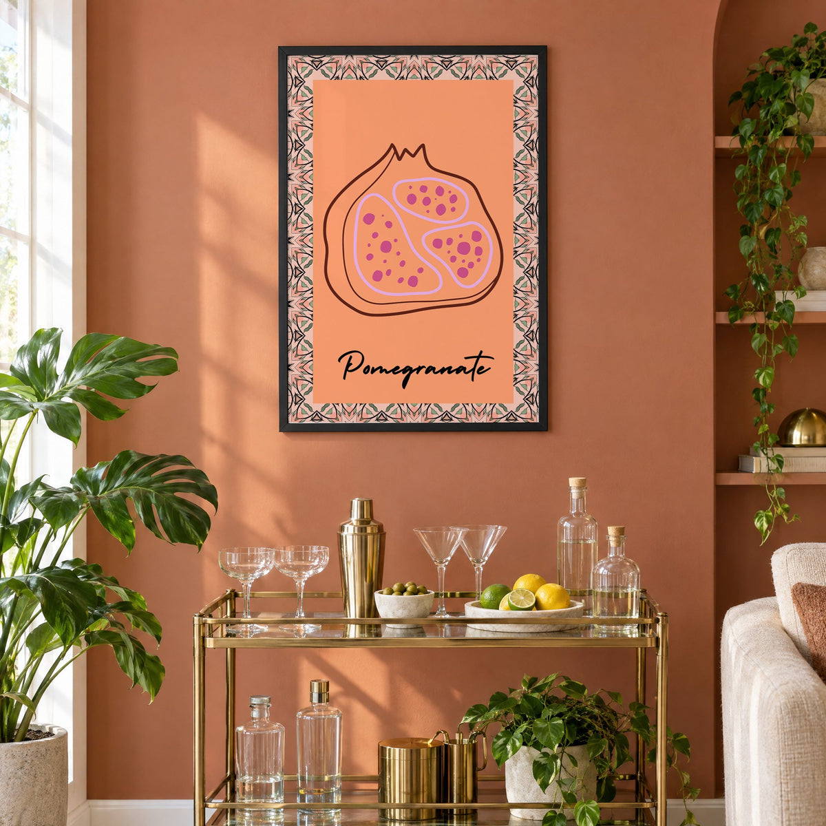 Pomegranate line-art kaleidoscope border print in a black frame on a terracotta wall above a brass bar cart with coupes and citrus