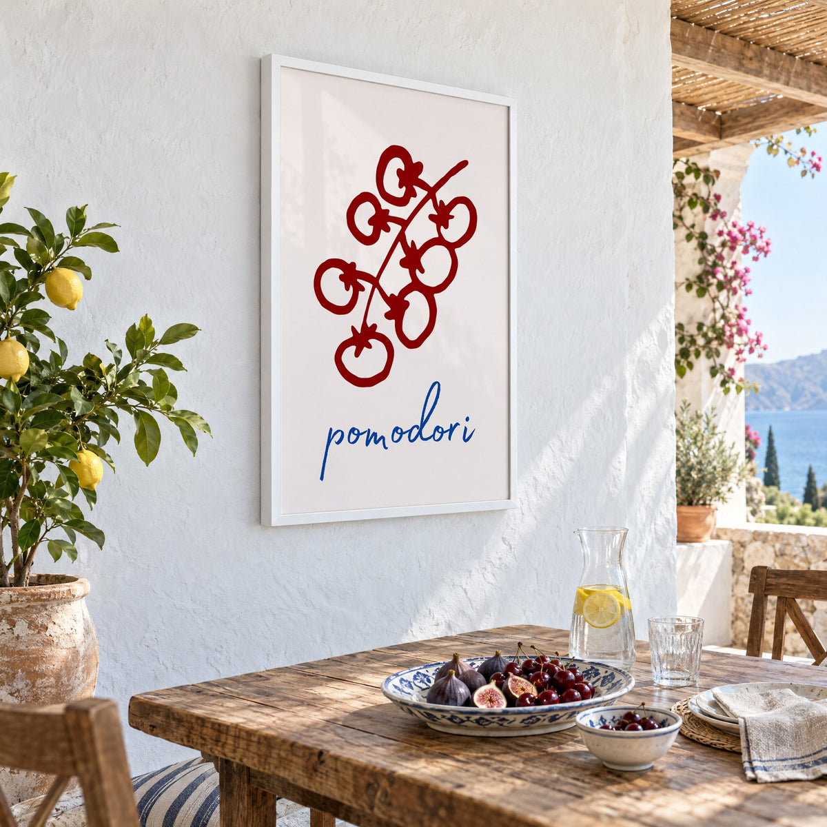 pomodori red cherry tomato vine print in a white frame on a whitewashed terrace wall above a lunch table with figs and cherries, seen at an angle