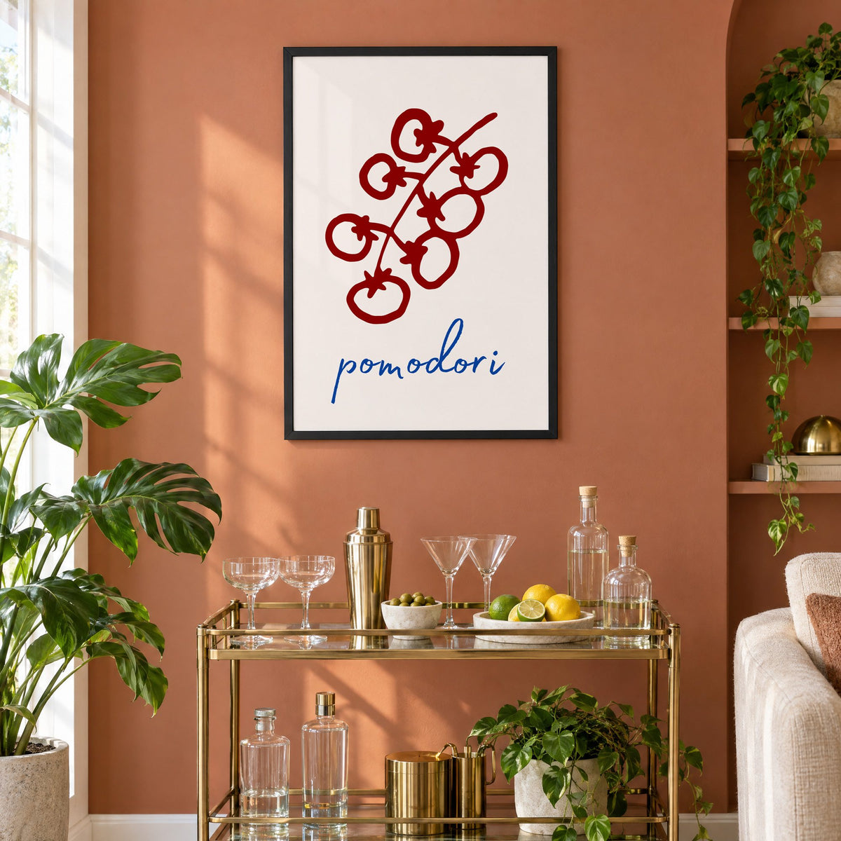 pomodori red cherry tomato vine print in a black frame on a terracotta wall above a brass bar cart with coupes and citrus