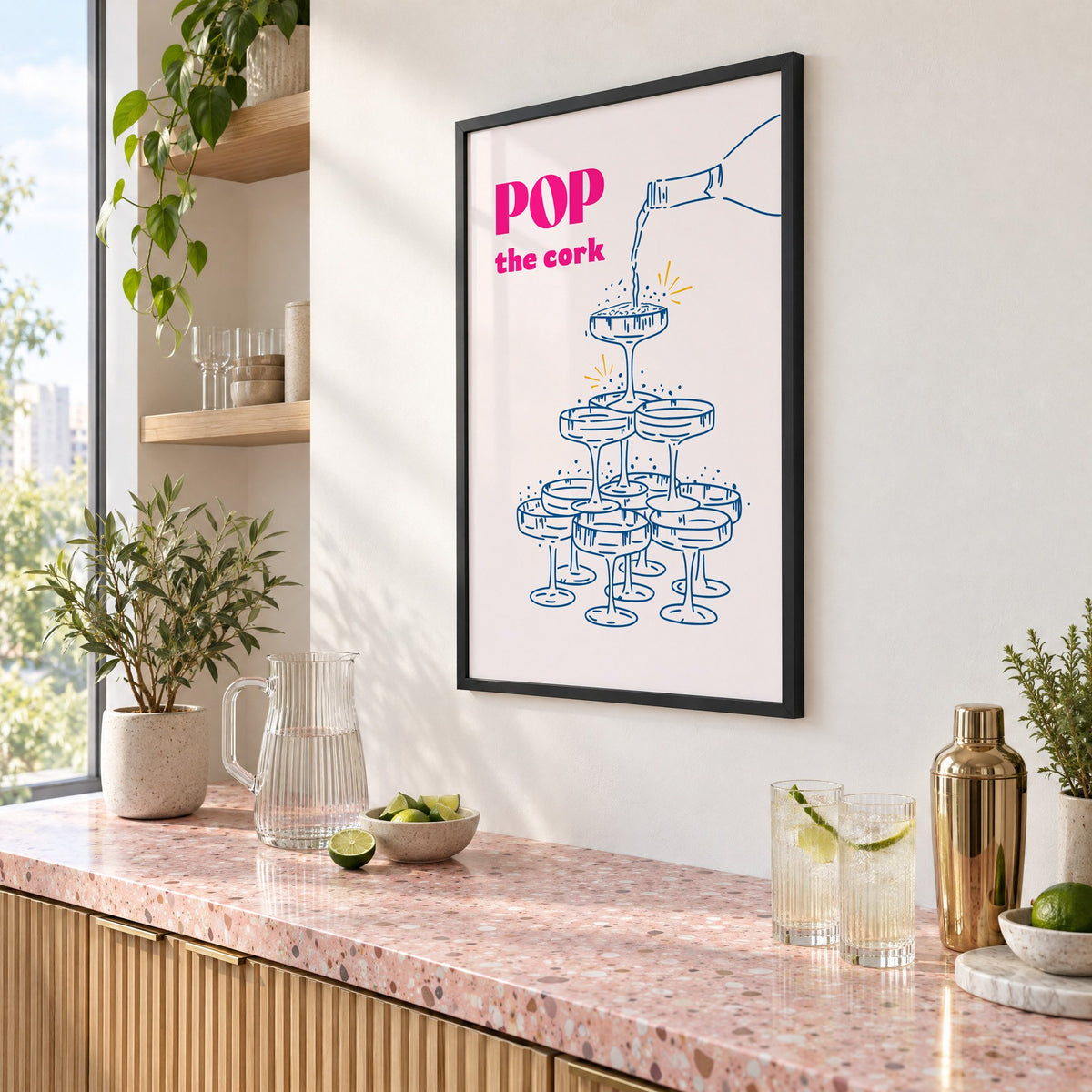 Pop the cork champagne tower print in a black frame above a pink terrazzo cocktail counter with limes, seen at an angle