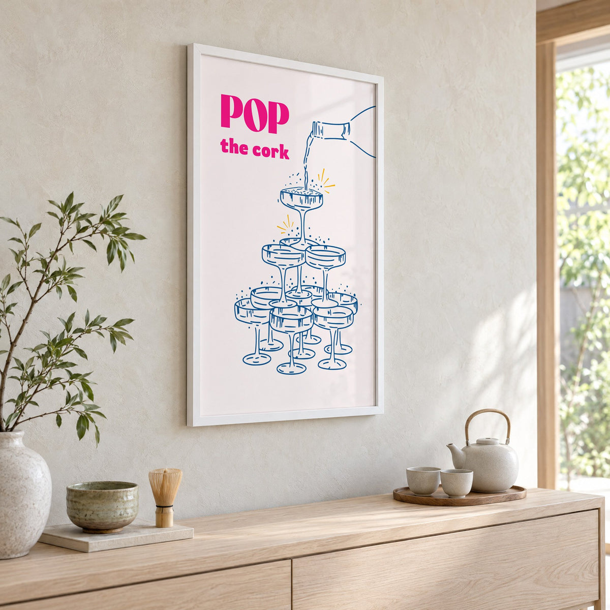 Pop the cork champagne tower print in a white frame above a pale wood console with a matcha tea set