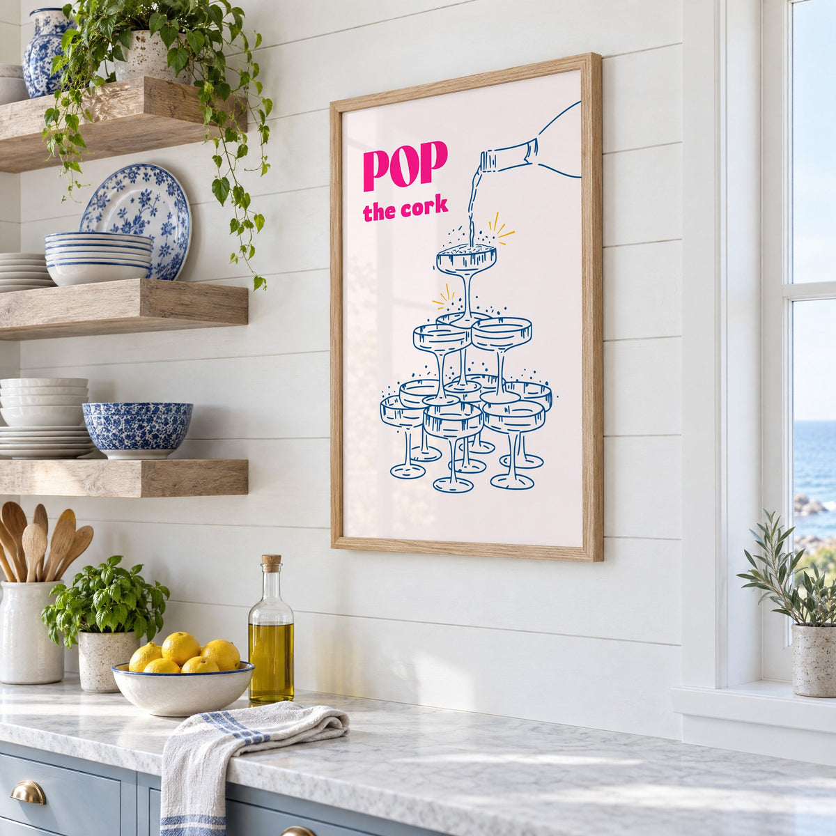 Pop the cork champagne tower print in an oak frame in a white coastal kitchen beside blue and white plates