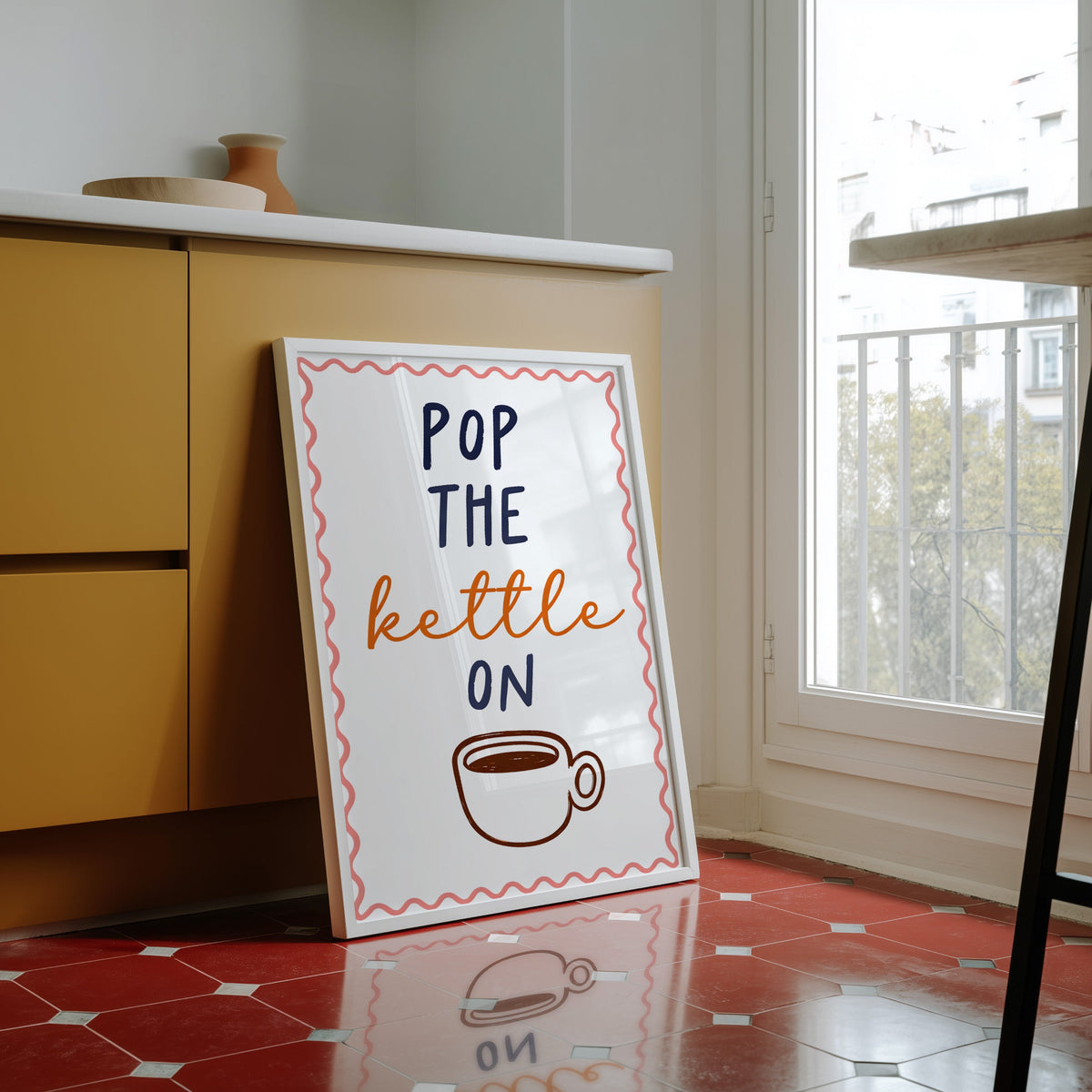 Pop the Kettle On print in a white frame against yellow cabinets on red tiles