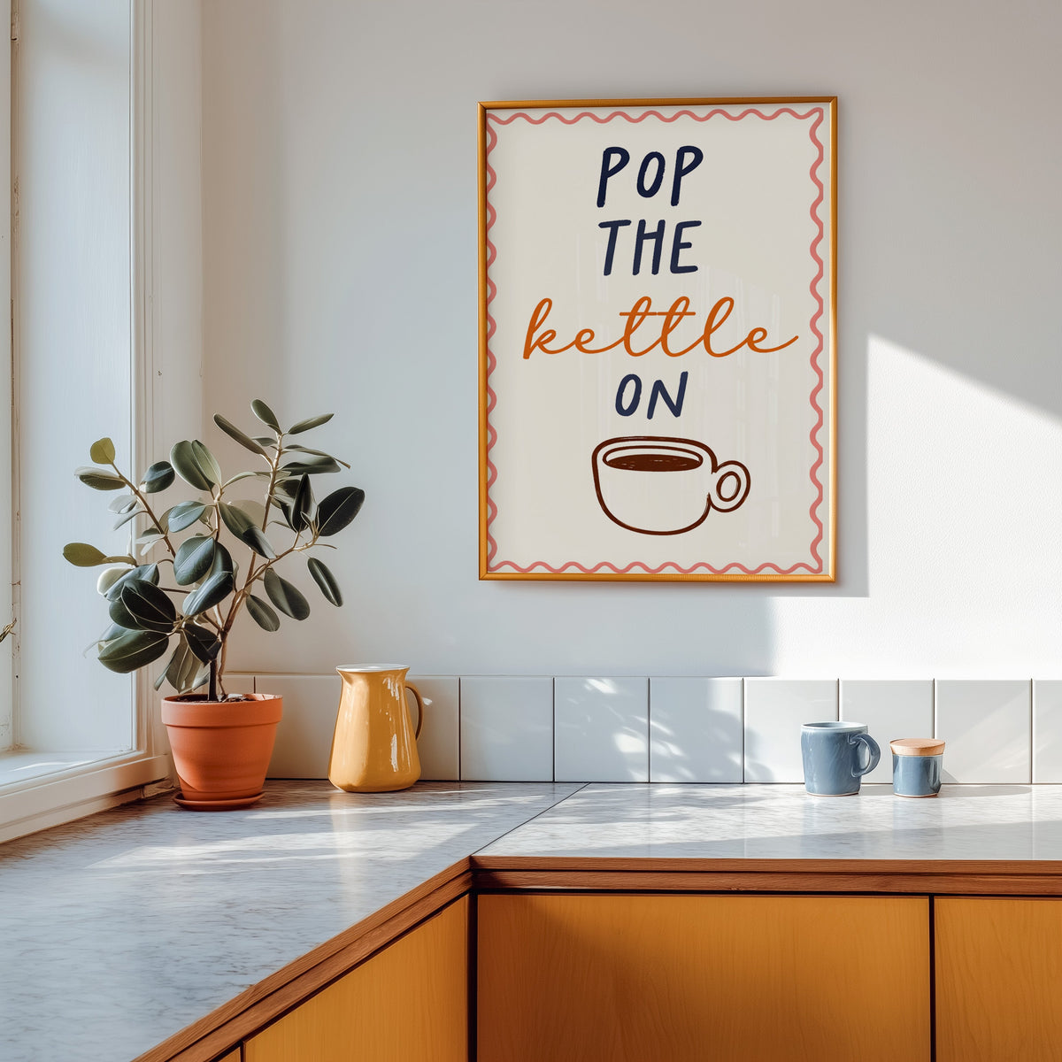 Pop the Kettle On print in a gold frame above a marble counter with a yellow jug