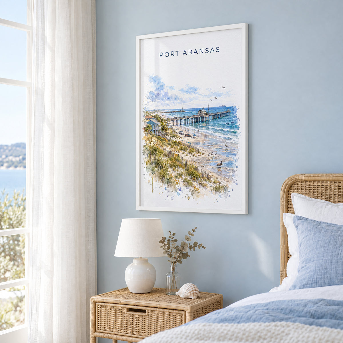 Port Aransas watercolor print in a white frame on a pale blue wall beside a rattan bed in a coastal bedroom