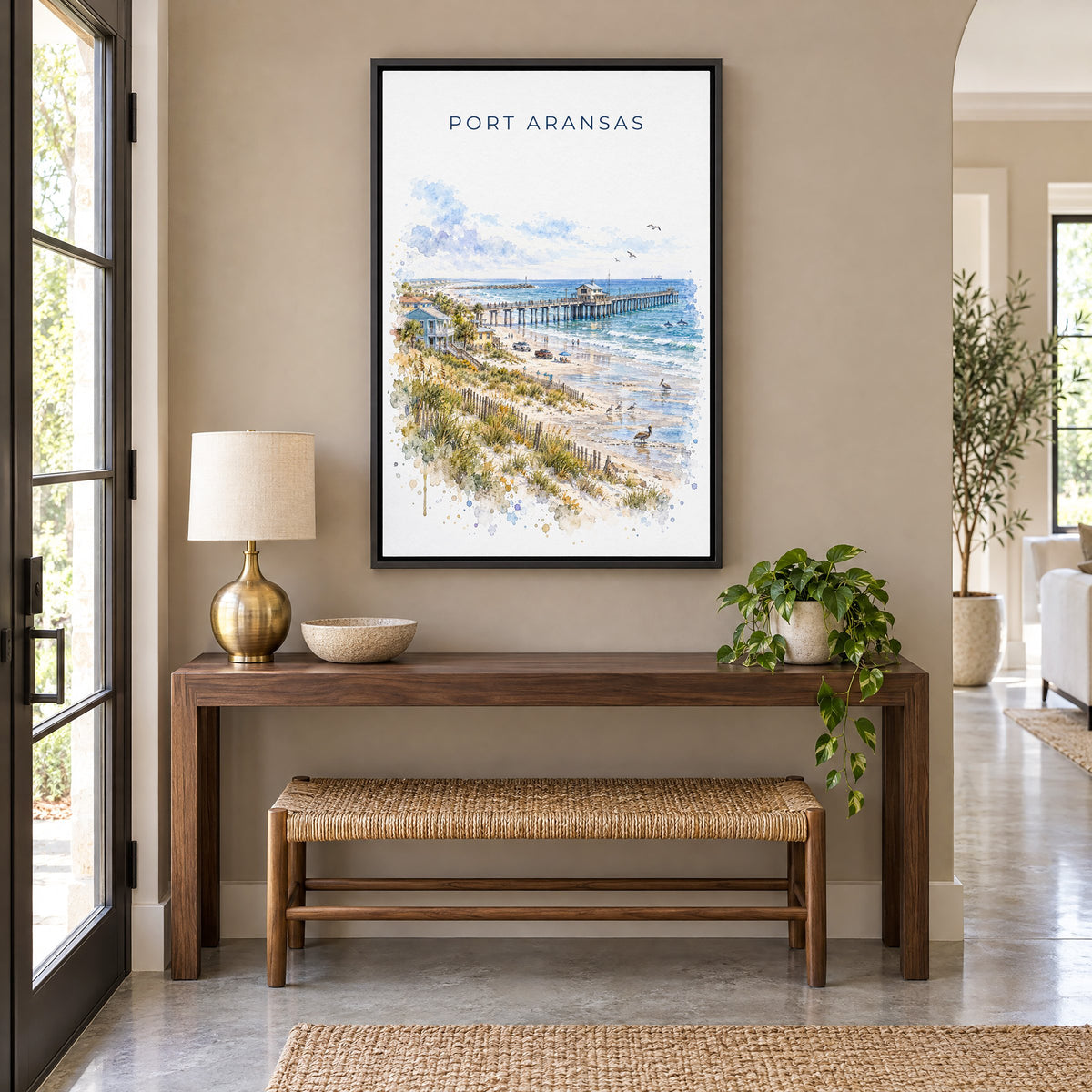 Port Aransas watercolor print as a black floater canvas above a walnut console and woven bench in an entryway