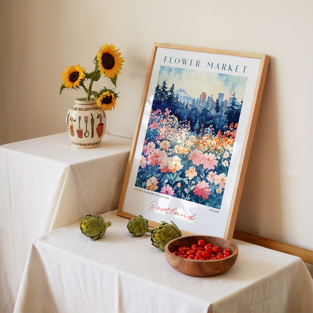 Portland flower market print in an oak frame leaning on a linen-draped table beside a vase of sunflowers