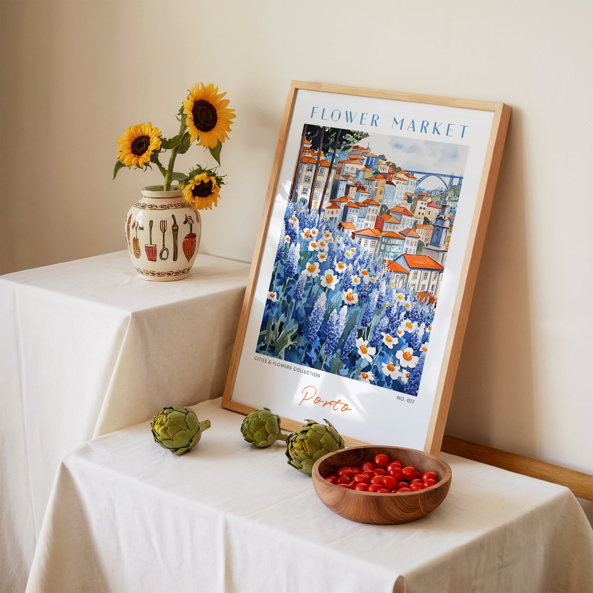 Porto flower market print in an oak frame leaning on a linen-draped table beside a vase of sunflowers