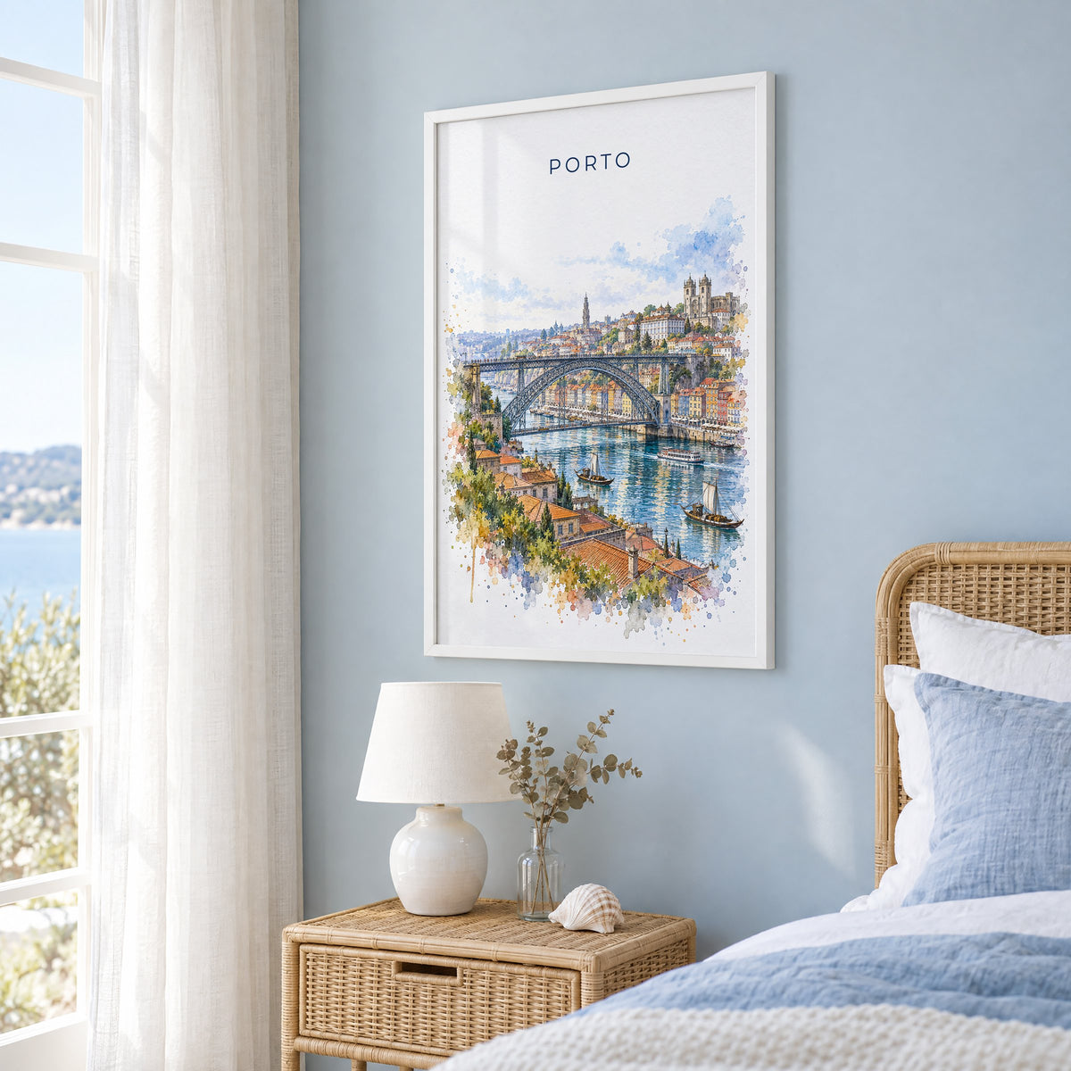 Porto watercolor print in a white frame on a pale blue wall beside a rattan bed in a coastal bedroom