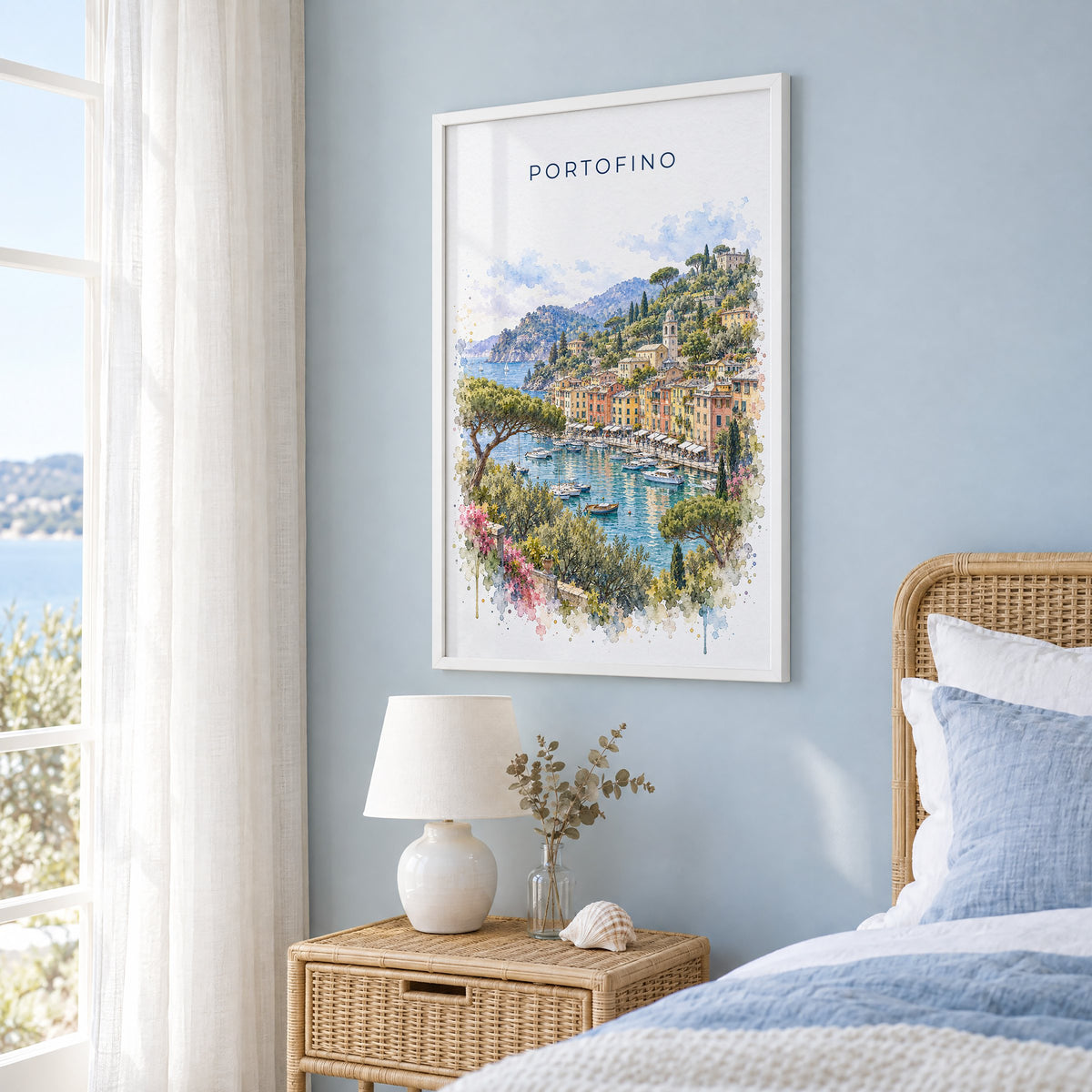 Portofino watercolor print in a white frame on a pale blue wall beside a rattan bed in a coastal bedroom