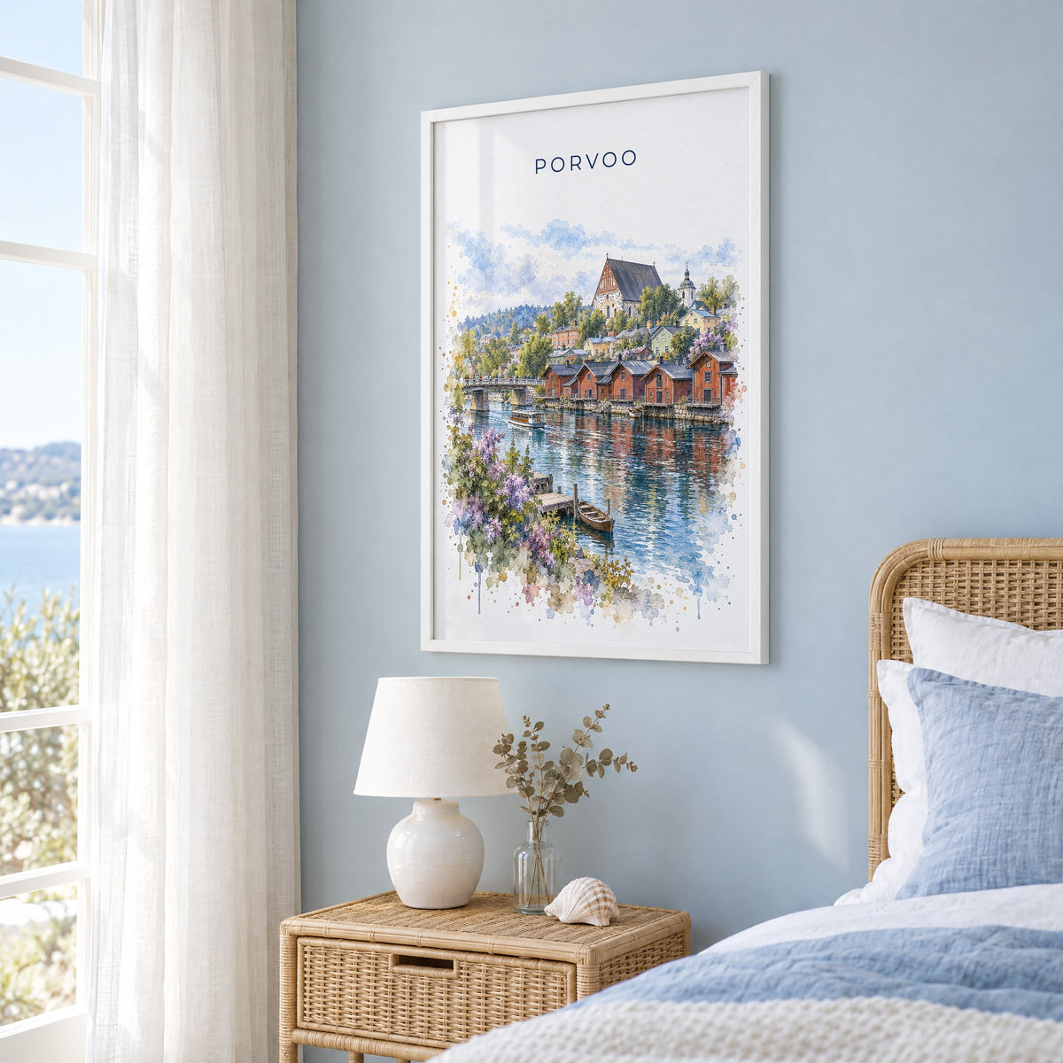 Porvoo watercolor print in a white frame on a pale blue wall beside a rattan bed in a coastal bedroom