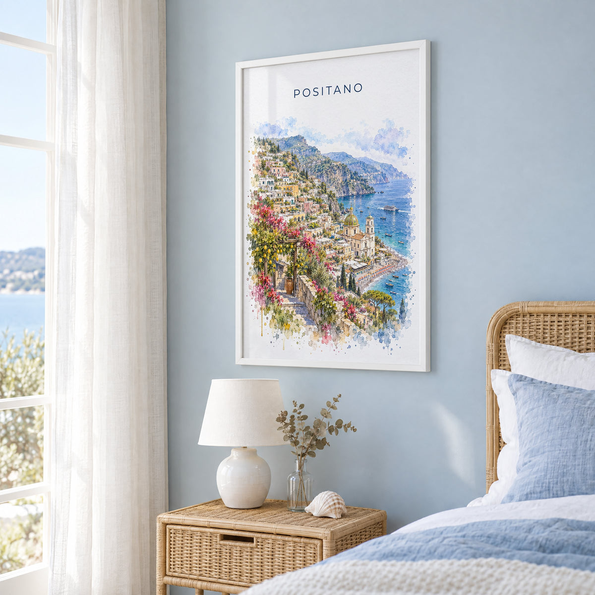 Positano watercolor print in a white frame on a pale blue wall beside a rattan bed in a coastal bedroom