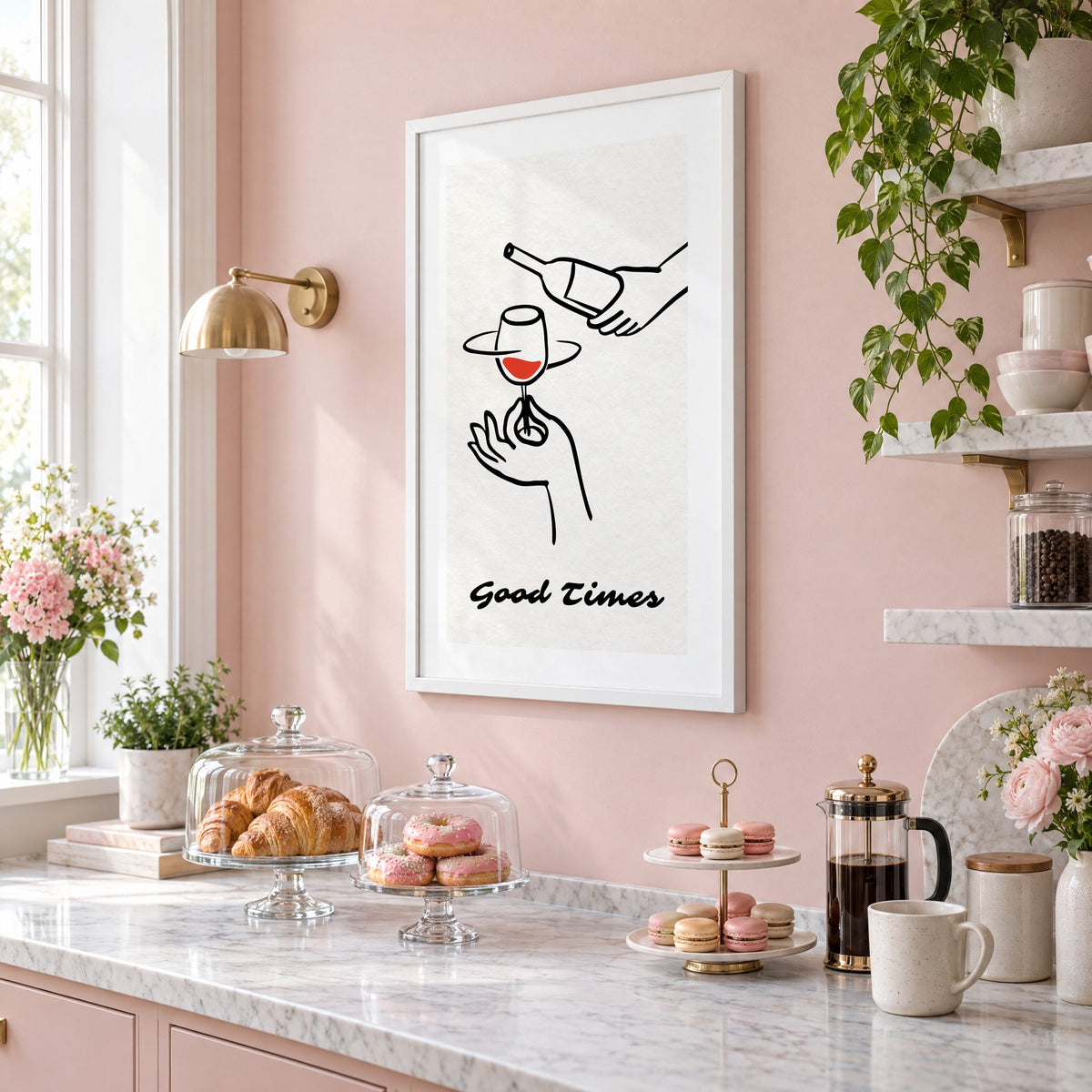 Good Times wine bottle and glass line print in a white frame on a blush pink wall above a patisserie counter with croissants and macarons, seen at an angle