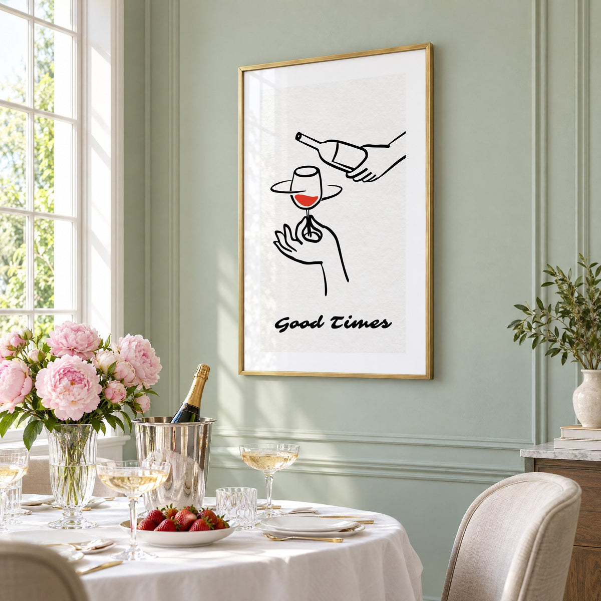 Good Times wine bottle and glass line print in a brass frame on a sage wall above a brunch table with champagne and peonies, seen at an angle