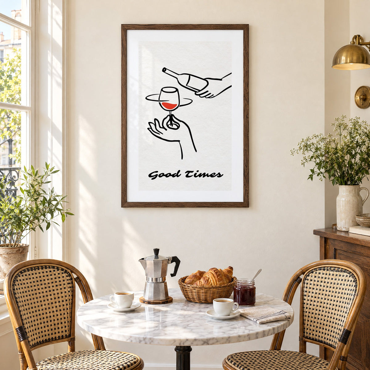 Good Times wine bottle and glass line print in a walnut frame above a marble bistro table with croissants and rattan chairs