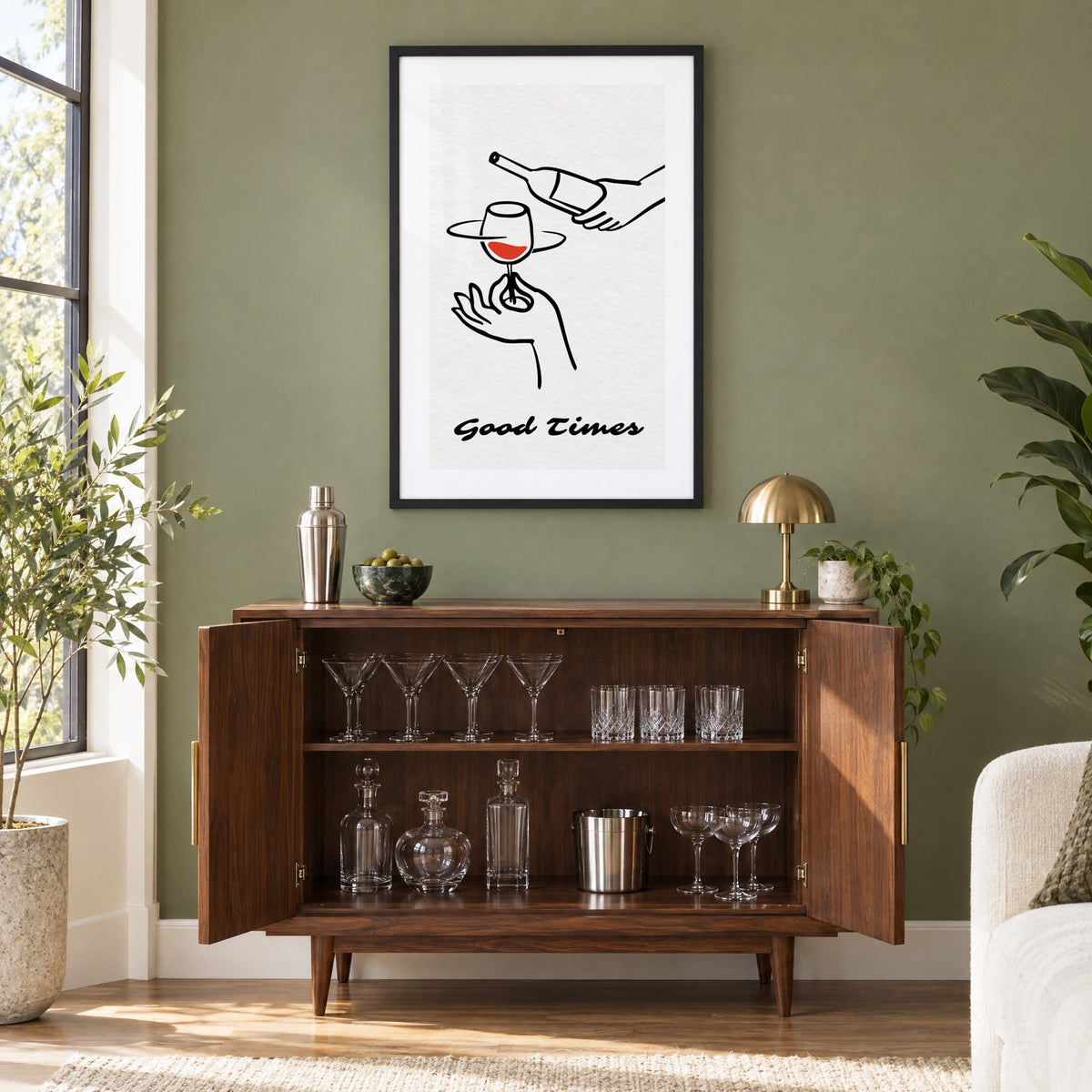 Good Times wine bottle and glass line print in a black frame on an olive green wall above a walnut bar cabinet with glassware
