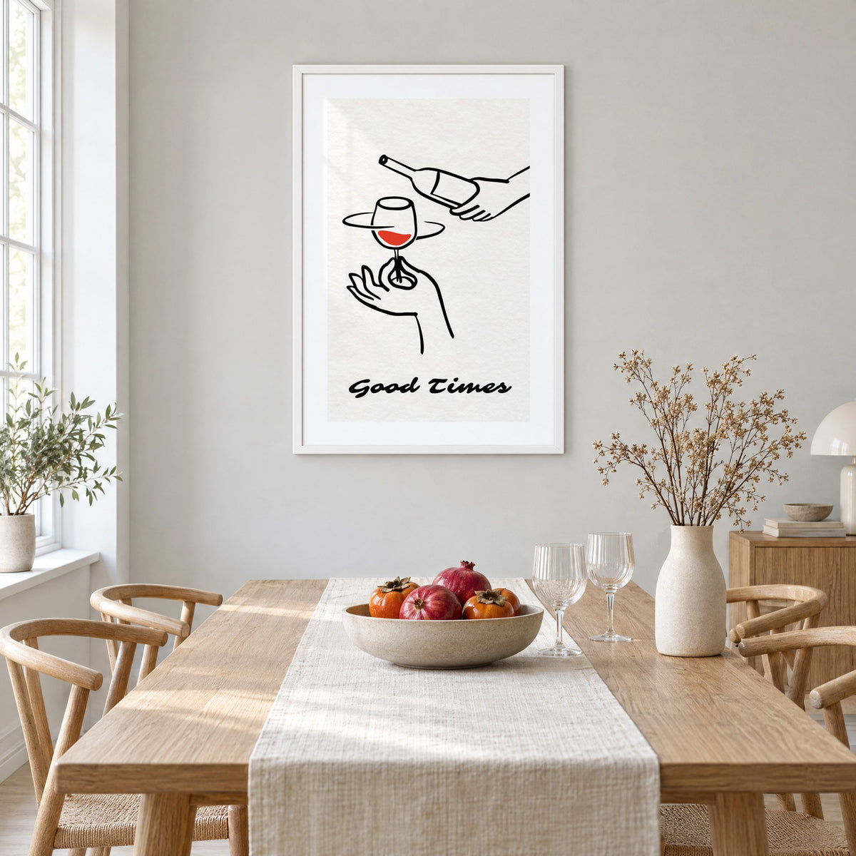 Good Times wine bottle and glass line print in a white frame above a light oak dining table with a linen runner and fruit bowl