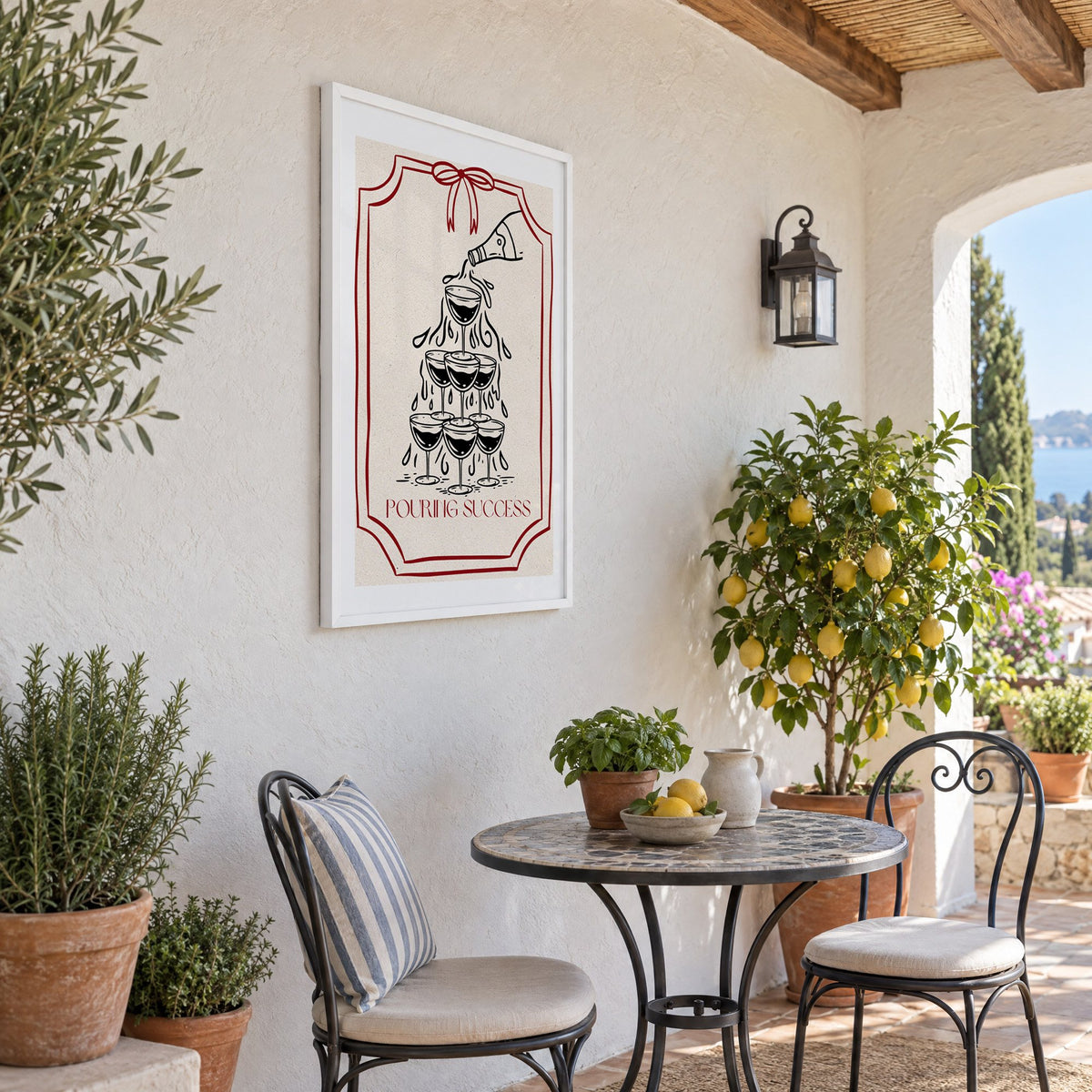 POURING SUCCESS champagne tower print in a white frame on a sunny patio wall beside a potted lemon tree