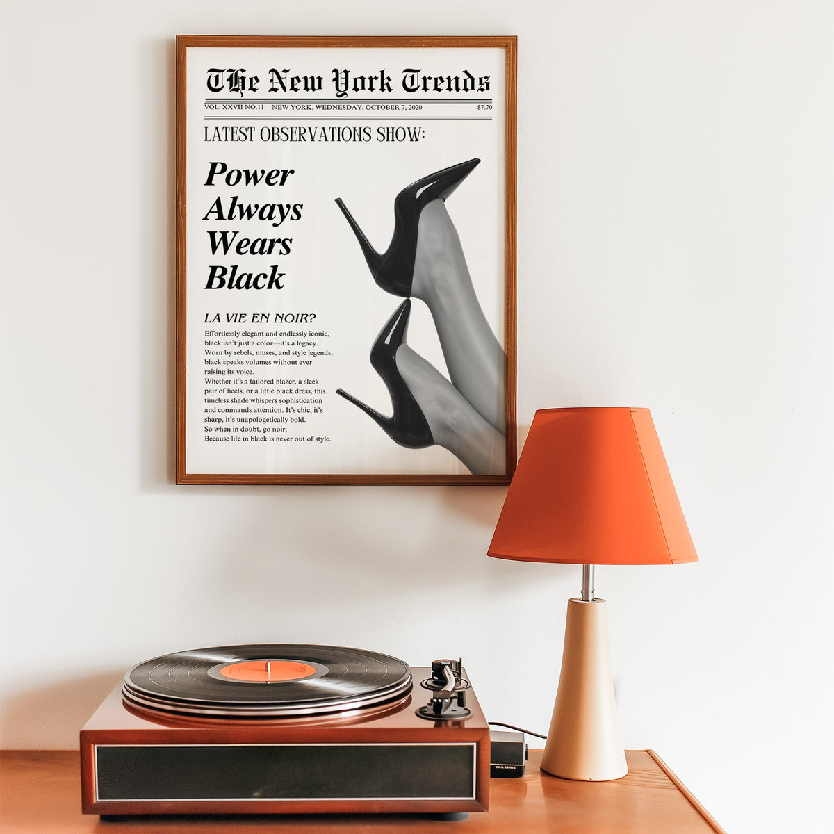 Two pairs of black heels mock newspaper print in a walnut frame above a record player and orange lamp